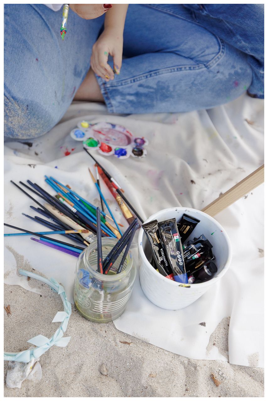 Glass jars and containers filled with various art supplies and drawing tools on white fabric.