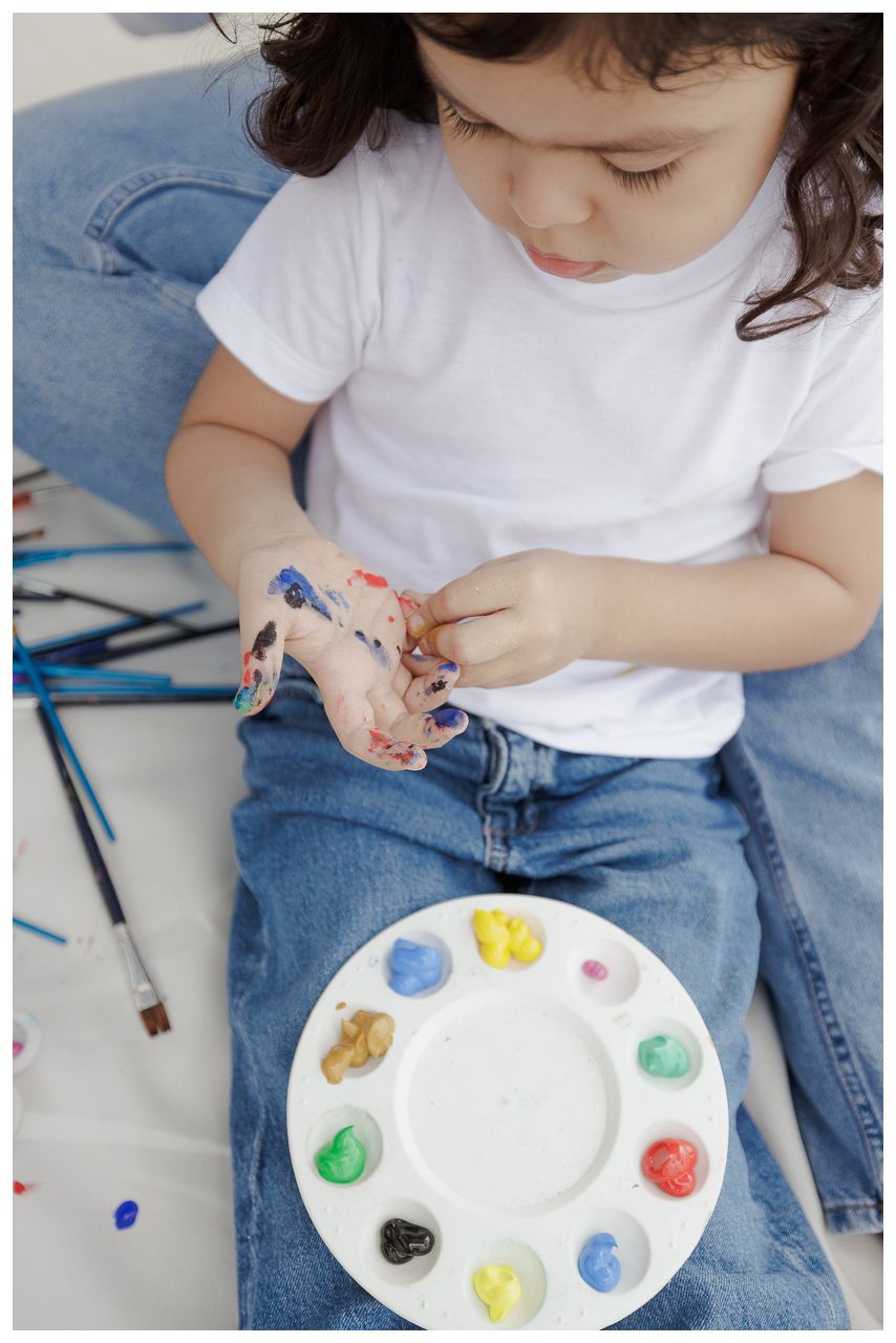 A person in a white t-shirt and jeans holds a paint palette with colorful paint dots arranged around the edge.
