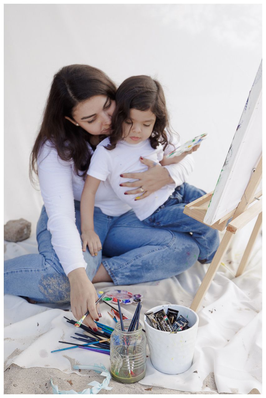 Two people in matching white shirts and jeans sit on the floor while working on an art project together.
