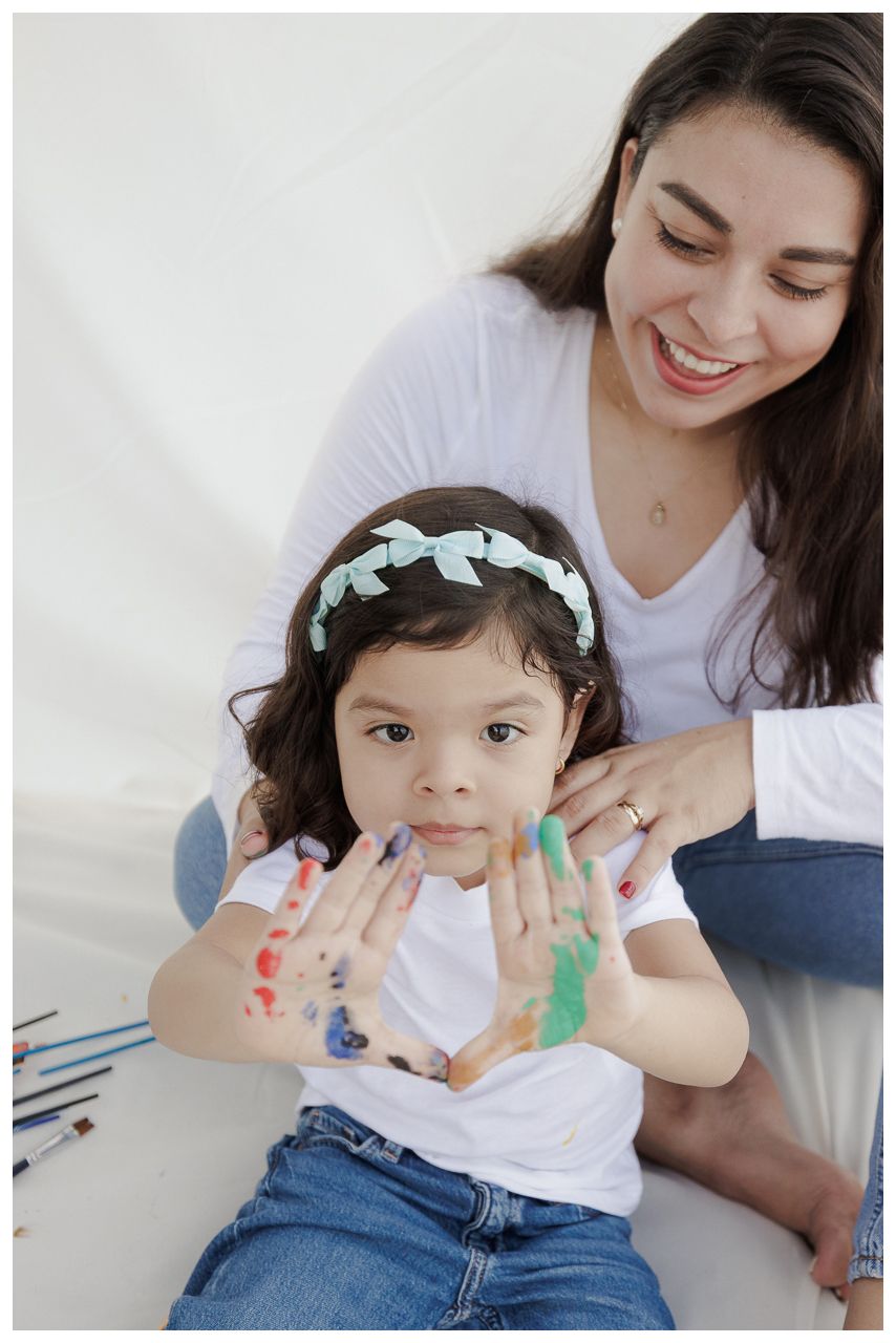 Parent and child wearing white shirts paint with colorful finger paints together in a bright indoor setting.