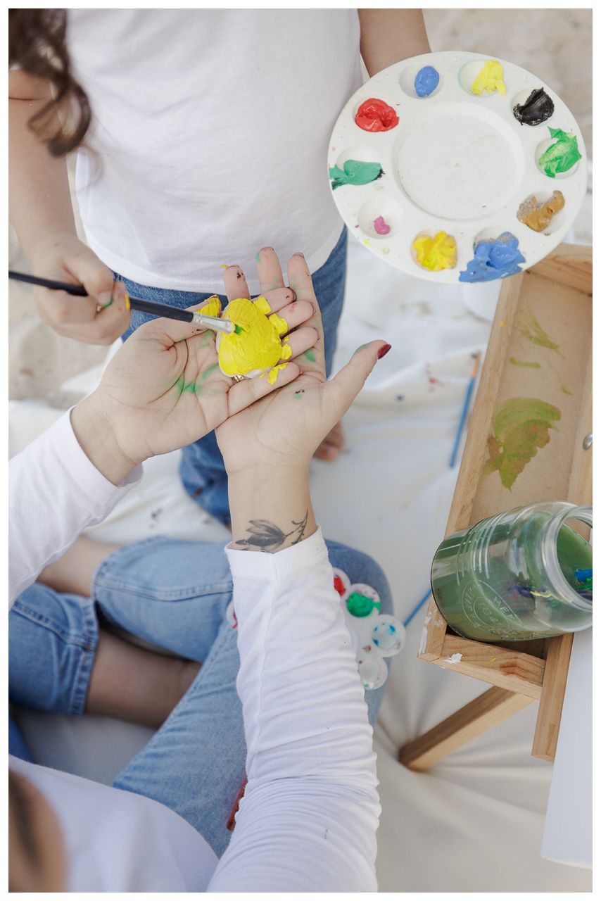 Artist holding paint palette and brush while working on canvas with colorful acrylic paints in studio setting.