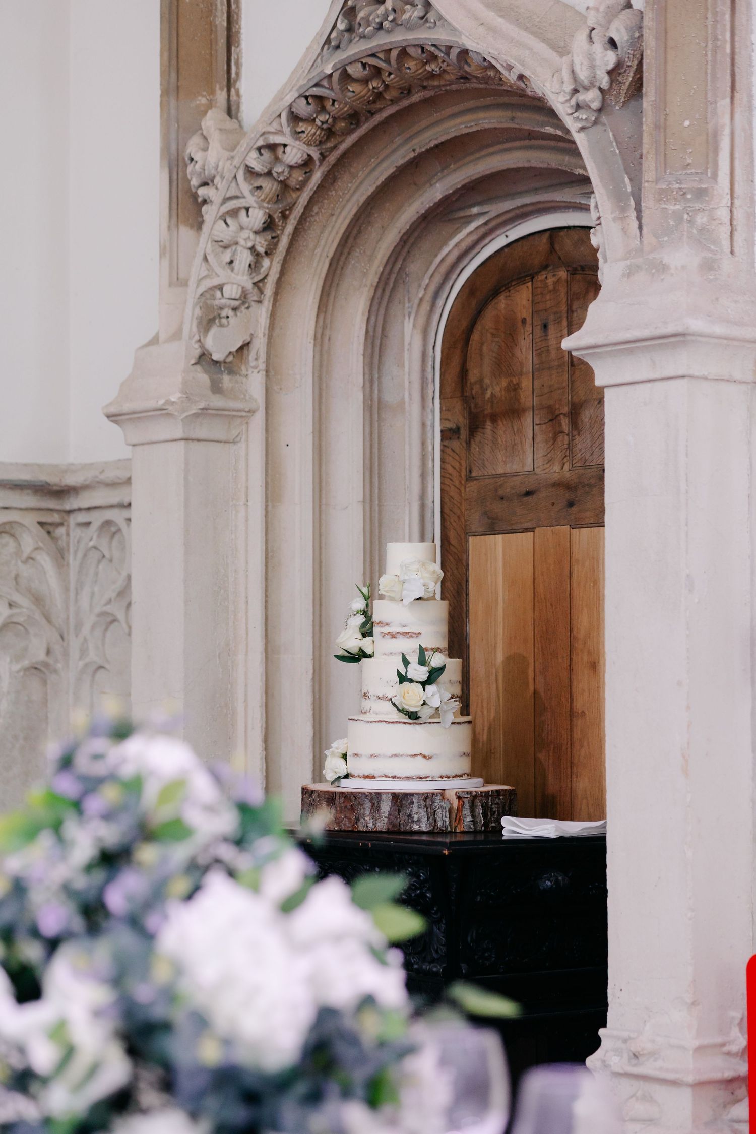 Gothic stone archways with ornate carvings line a church corridor with soft focus flowers in the foreground.