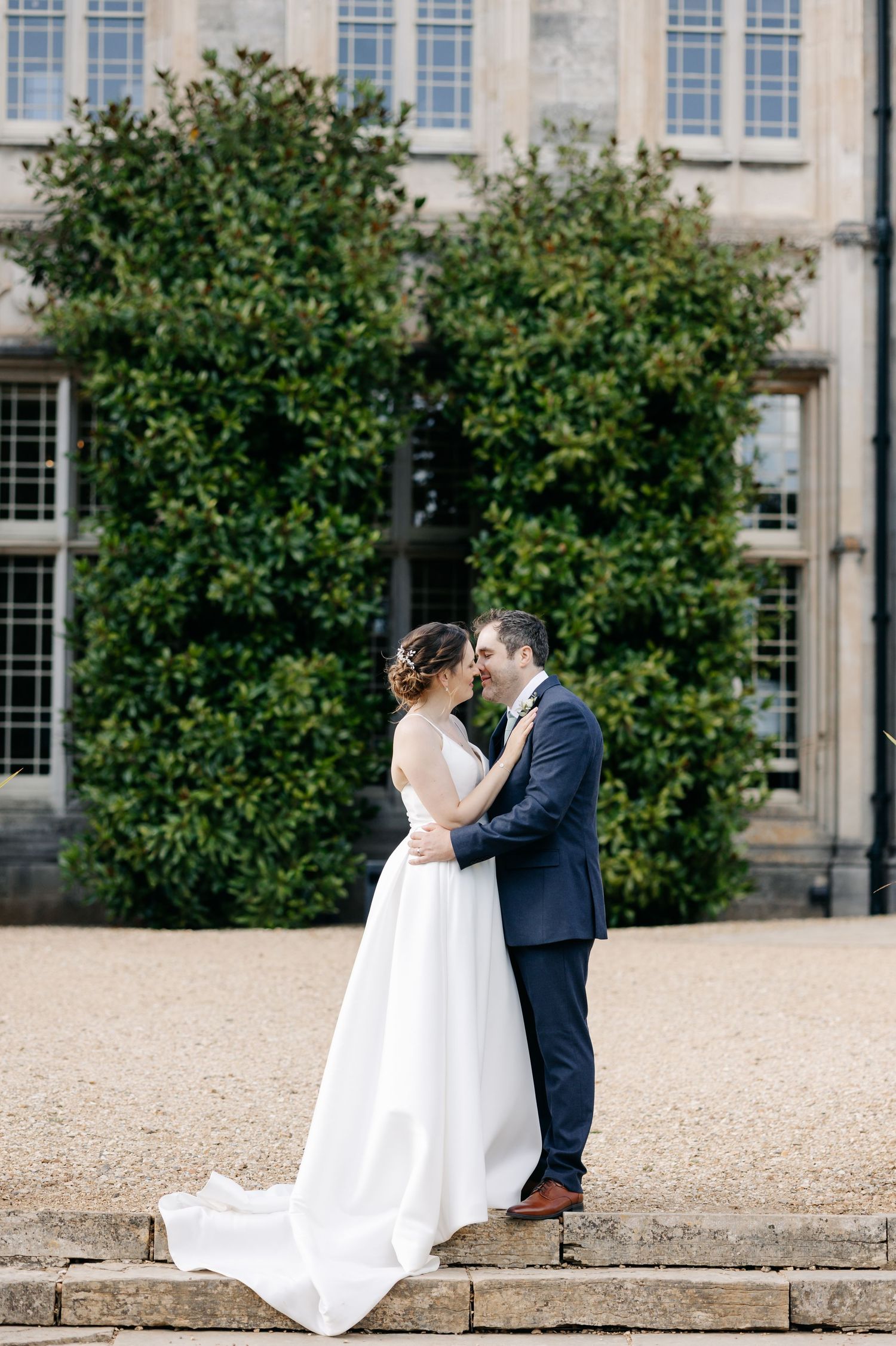 A romantic wedding couple shares intimate moments on stone steps outside an elegant building with blue windows.