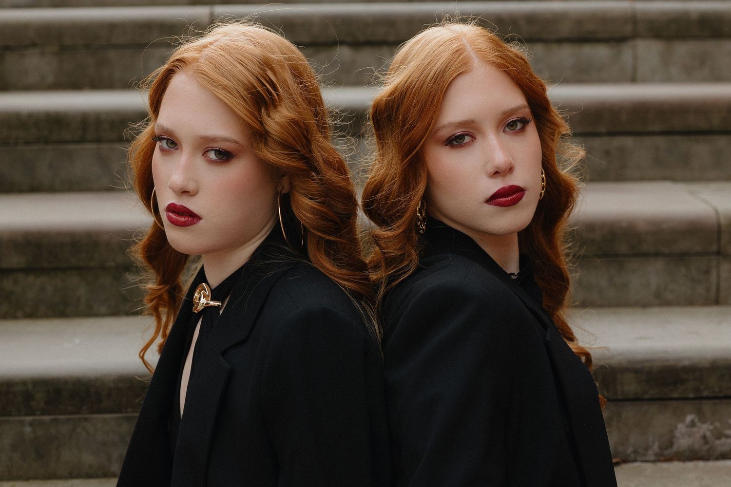 A person with red hair and red lipstick poses on stone steps in a vintage-inspired fashion photoshoot.