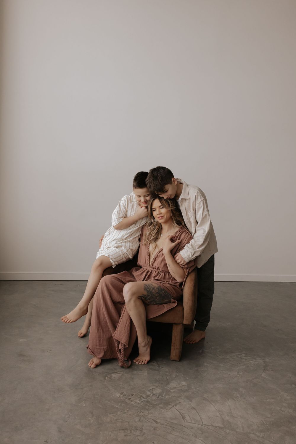 A couple shares an intimate moment while sitting together on a brown armchair in a minimalist setting.