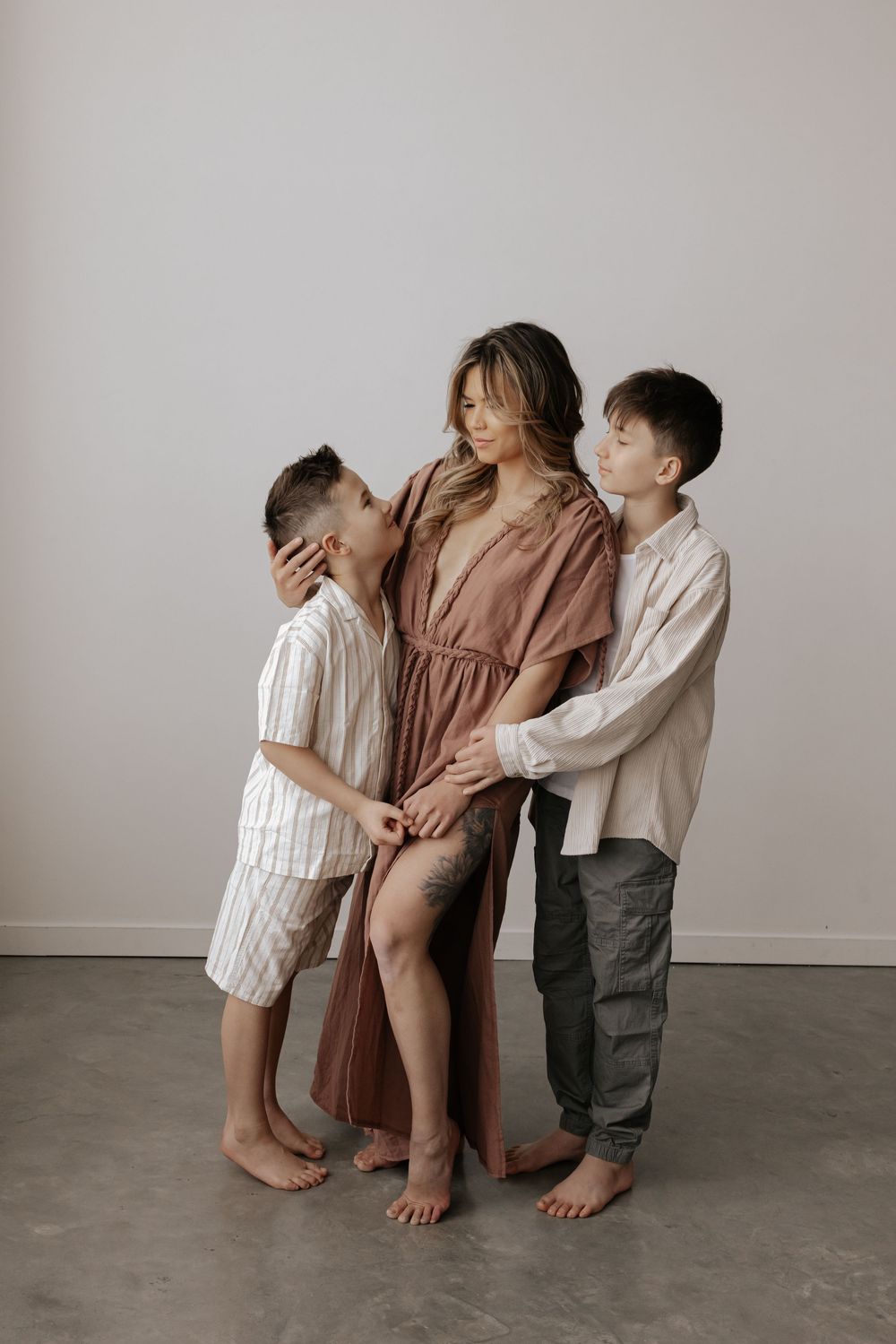 Three children in casual clothing pose playfully against a neutral wall in a minimalist setting.