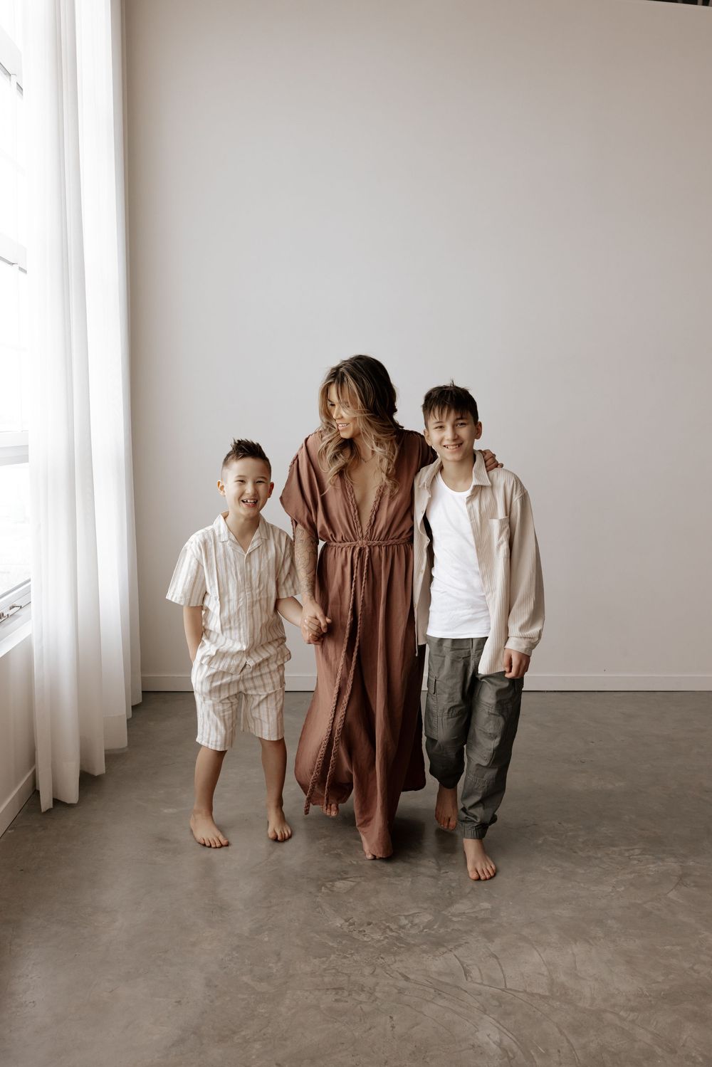 Family in coordinated neutral outfits standing together barefoot against white wall in minimalist setting.