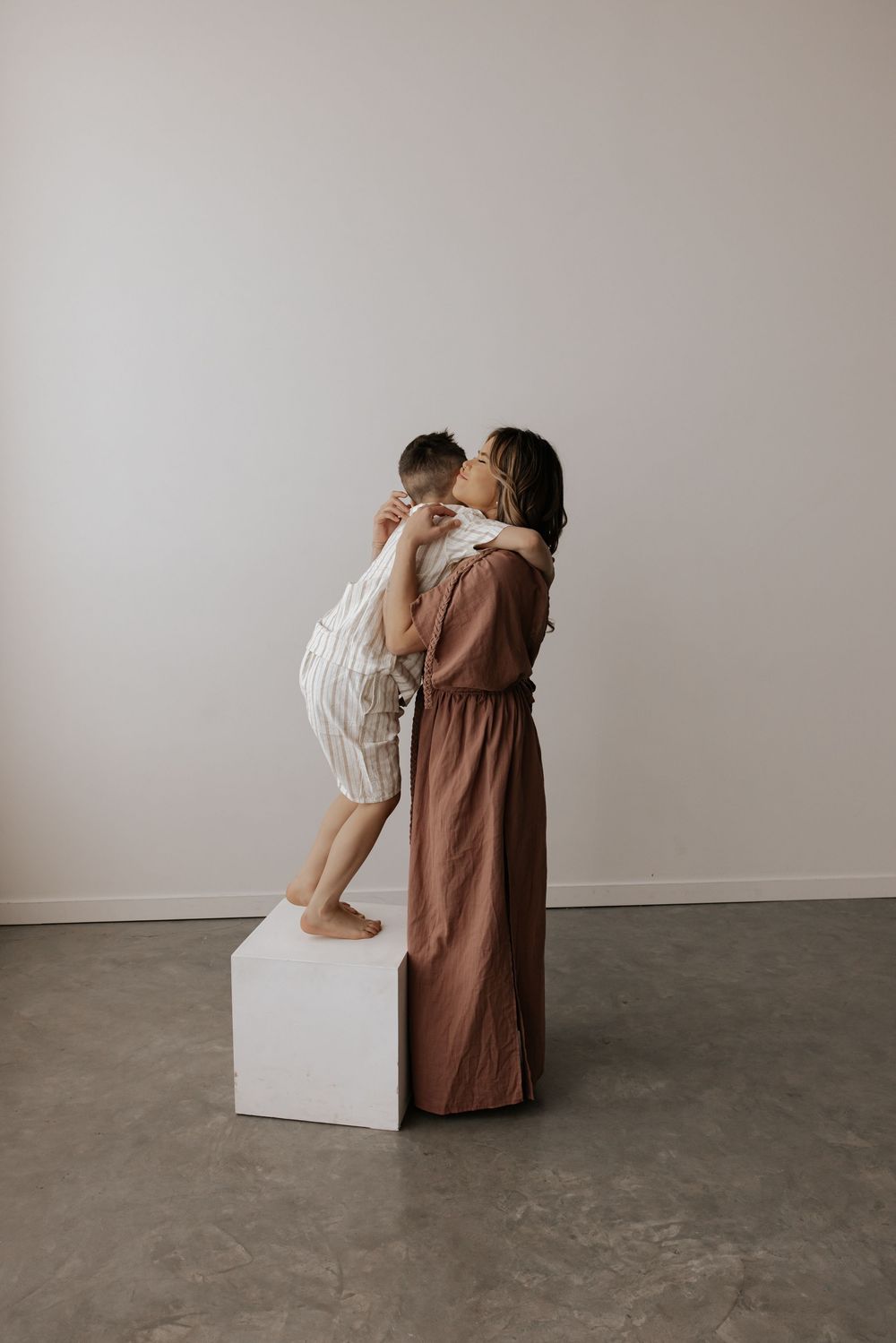 Intimate moment captured with brown dress and white outfit against minimal backdrop with white cube.