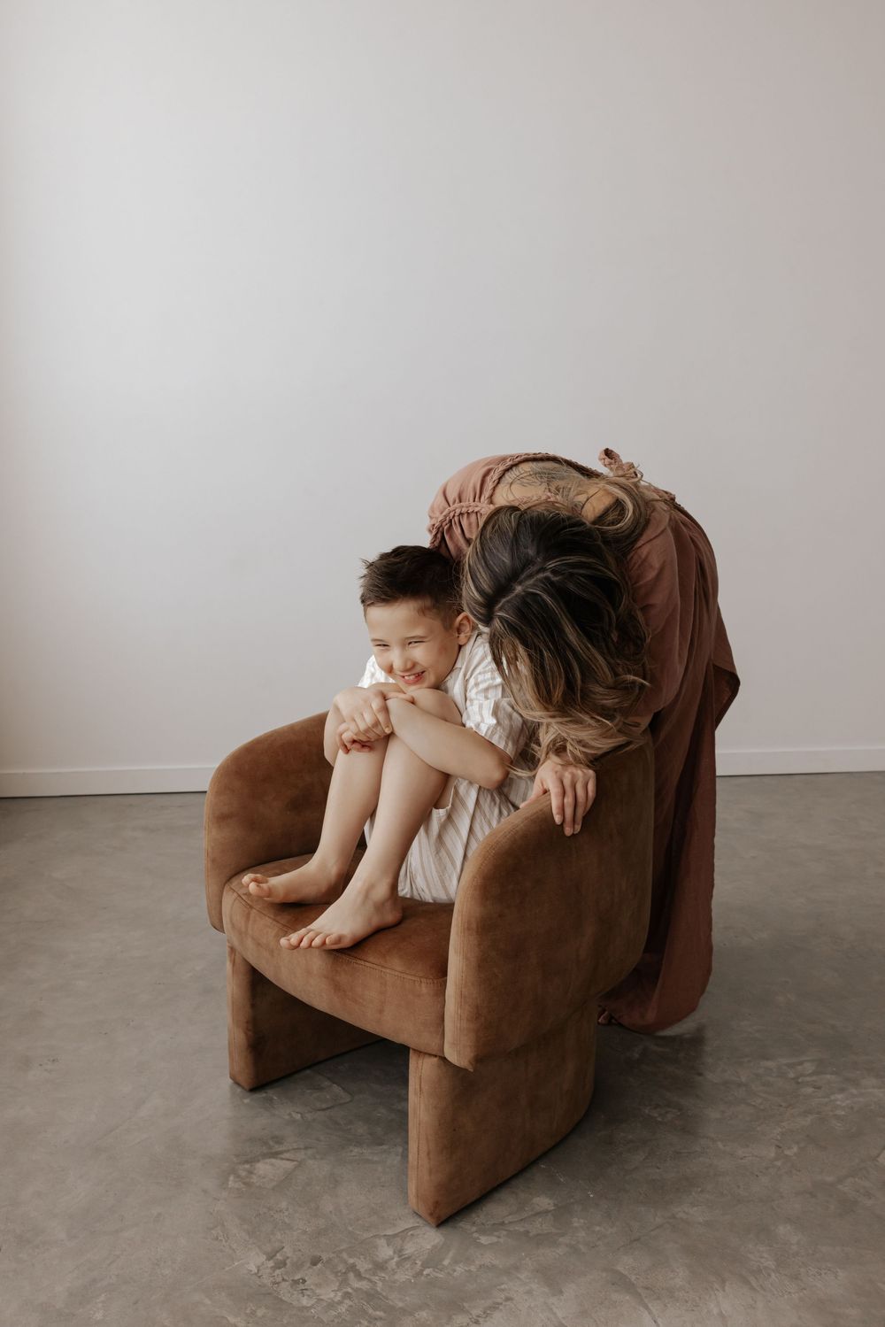 Two people lounge comfortably on a plush brown armchair in a bright, minimalist room.