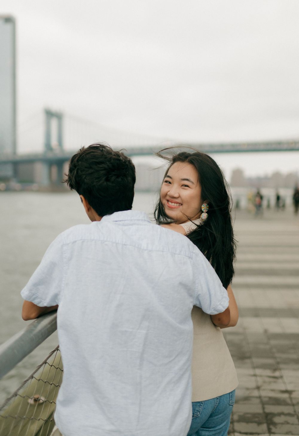 Romantic couple sharing a tender moment by the waterfront with urban architecture in the distance.