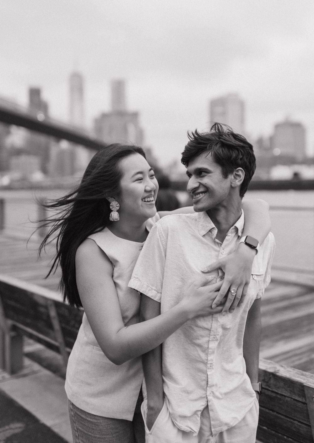 A joyful couple shares intimate laughs while posing against a city skyline in black and white.