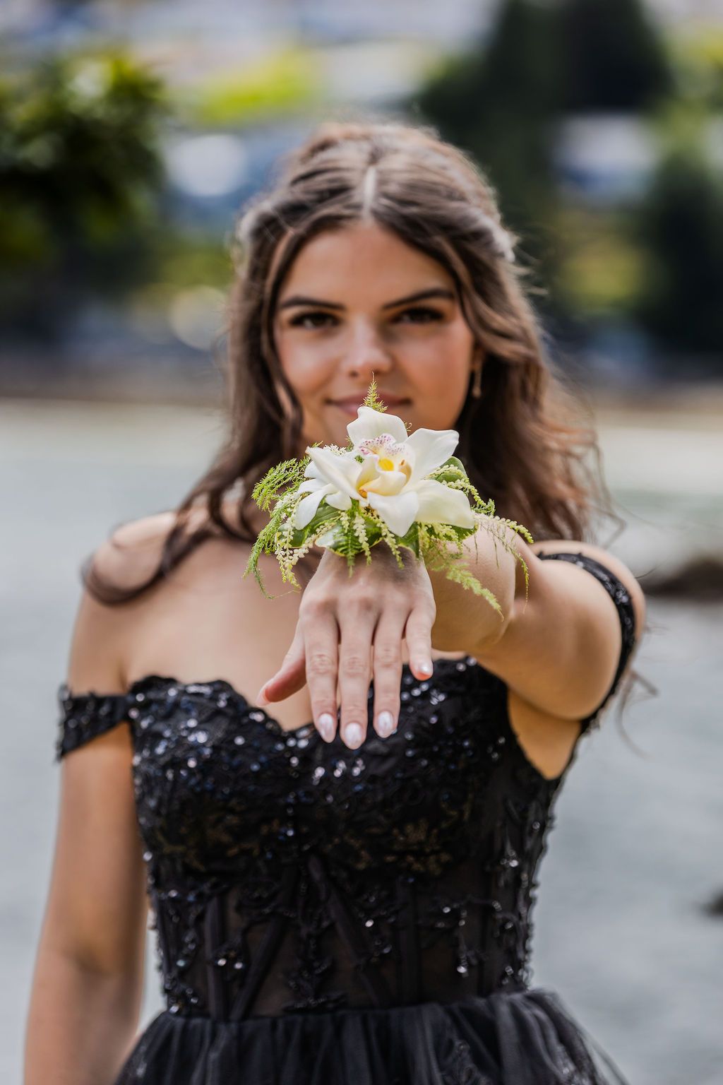 Young woman in black sequin off-shoulder gown displaying white orchid wrist corsage at prom.