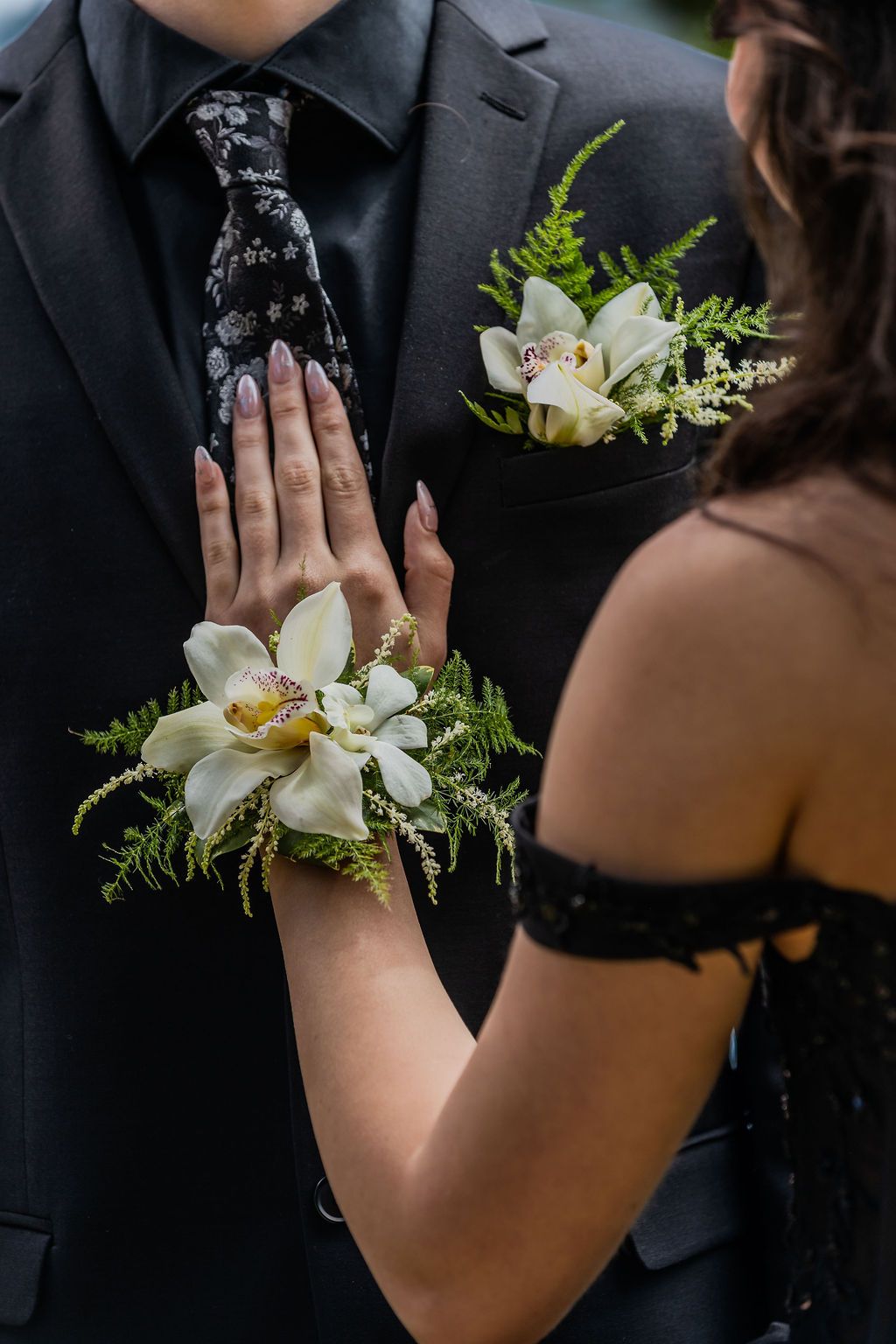 Prom couple showcasing matching white orchid corsage and boutonniere with fern accents.