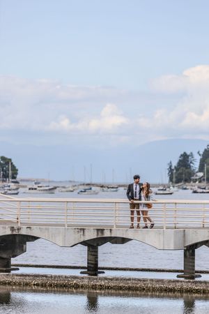 Prom couple standing together on a white bridge overlooking a marina on a sunny day.