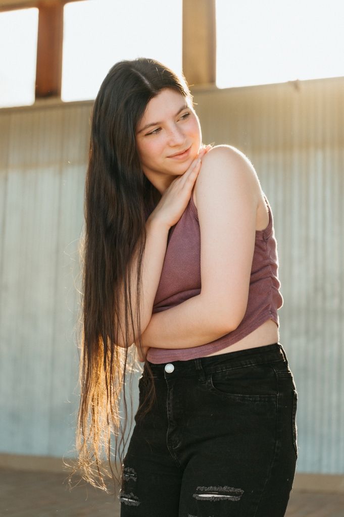 Young woman with long dark hair poses outdoors in a mauve crop top and black ripped jeans during golden hour.