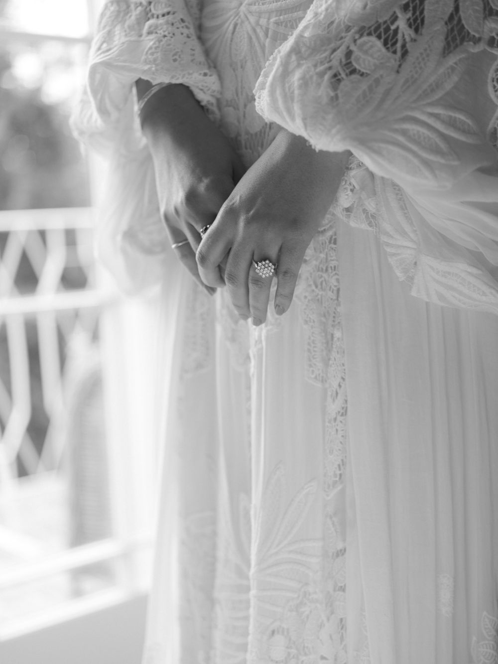 Black and white close-up of bride in lace wedding dress wearing a sparkling halo engagement ring.