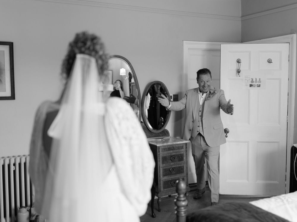 Black and white photo of a groom reacting emotionally to seeing his bride in her wedding dress and veil for the first time.