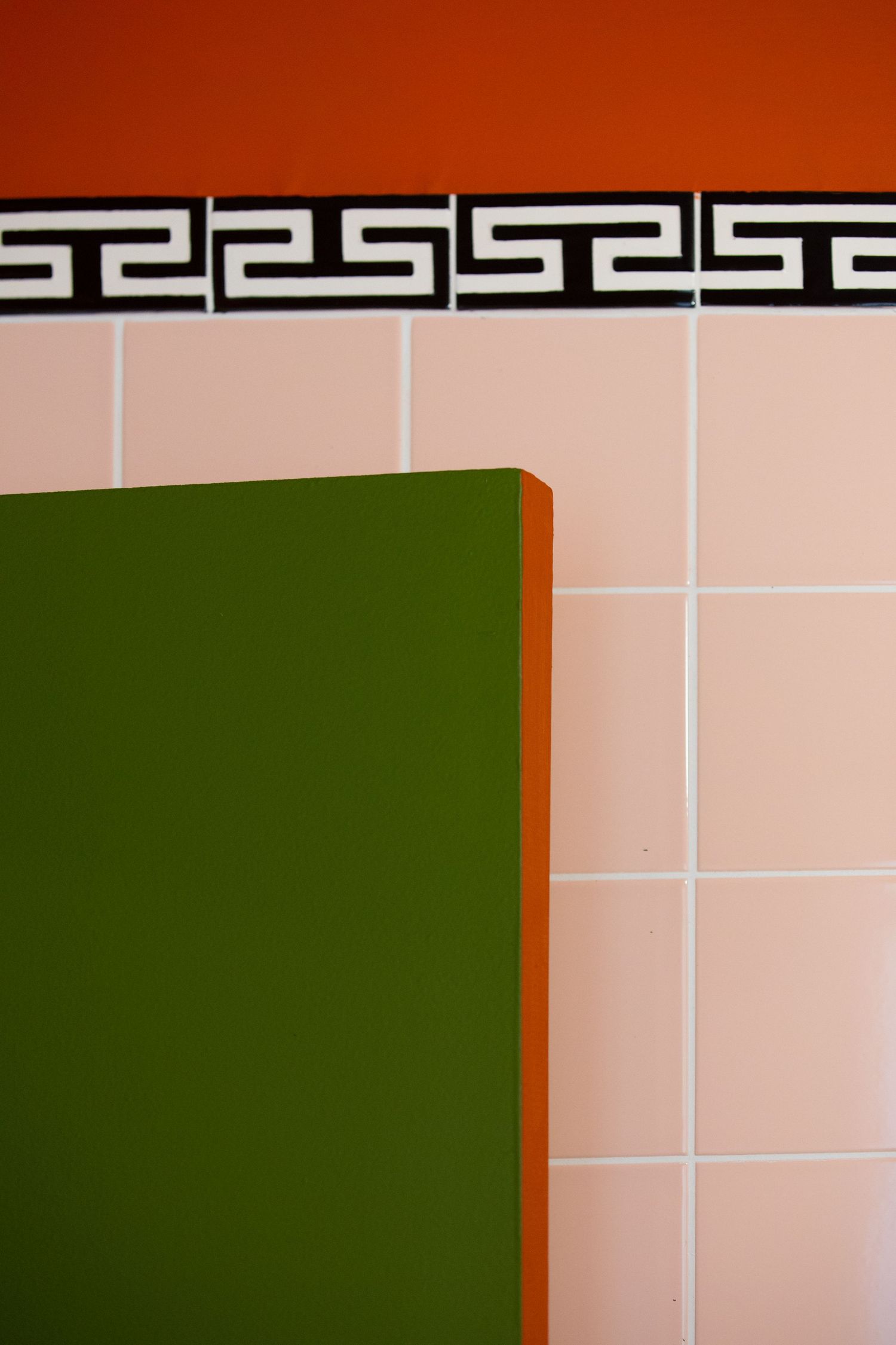 Abstract architectural detail showing pink tiles with dark border and green wall panel creating a geometric composition.