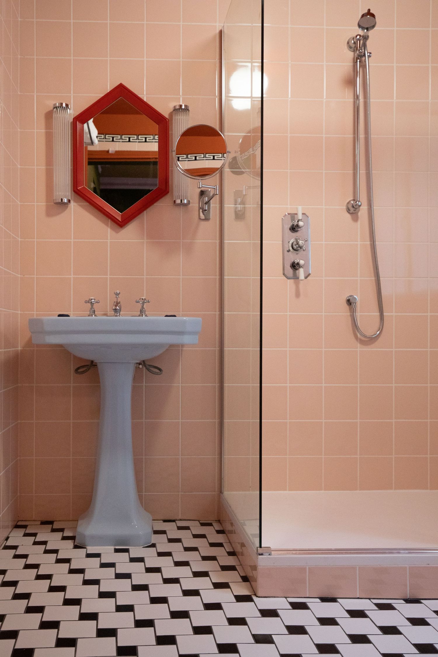 Vintage pink bathroom interior with black and white checkered floor, pedestal sink, and diamond-shaped mirrors on tiled walls.