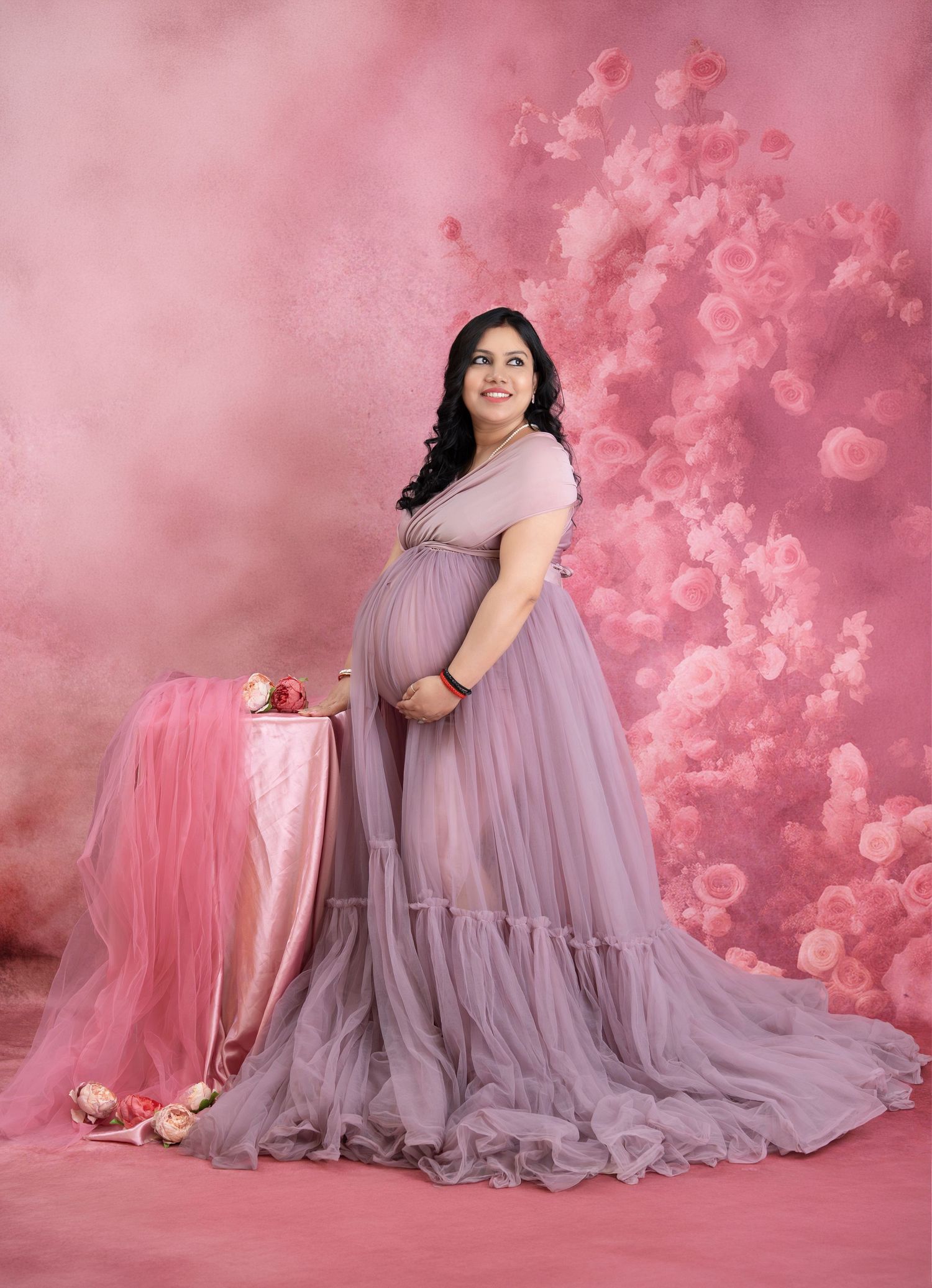 Studio maternity photoshoot in Hyderabad with mother in lavender gown against soft pink floral backdrop, calm and elegant setup