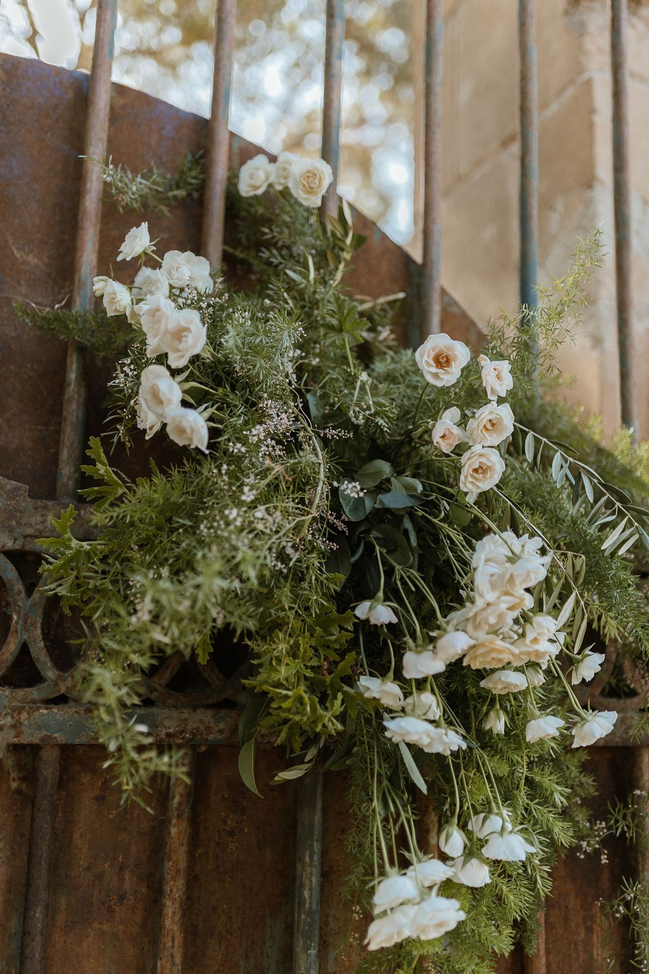 White roses and greenery floral arrangement draped over rustic iron garden gates for a wedding ceremony.