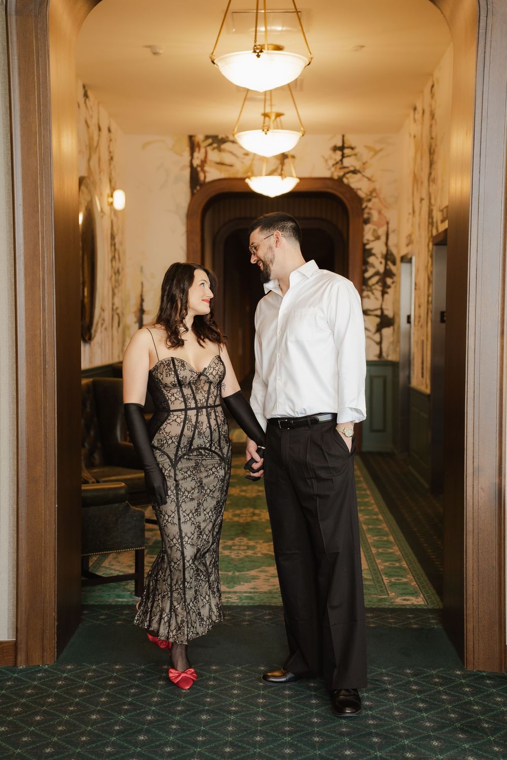 Couples dance in an elegant hallway with green carpet and ornate lighting fixtures during a formal event.