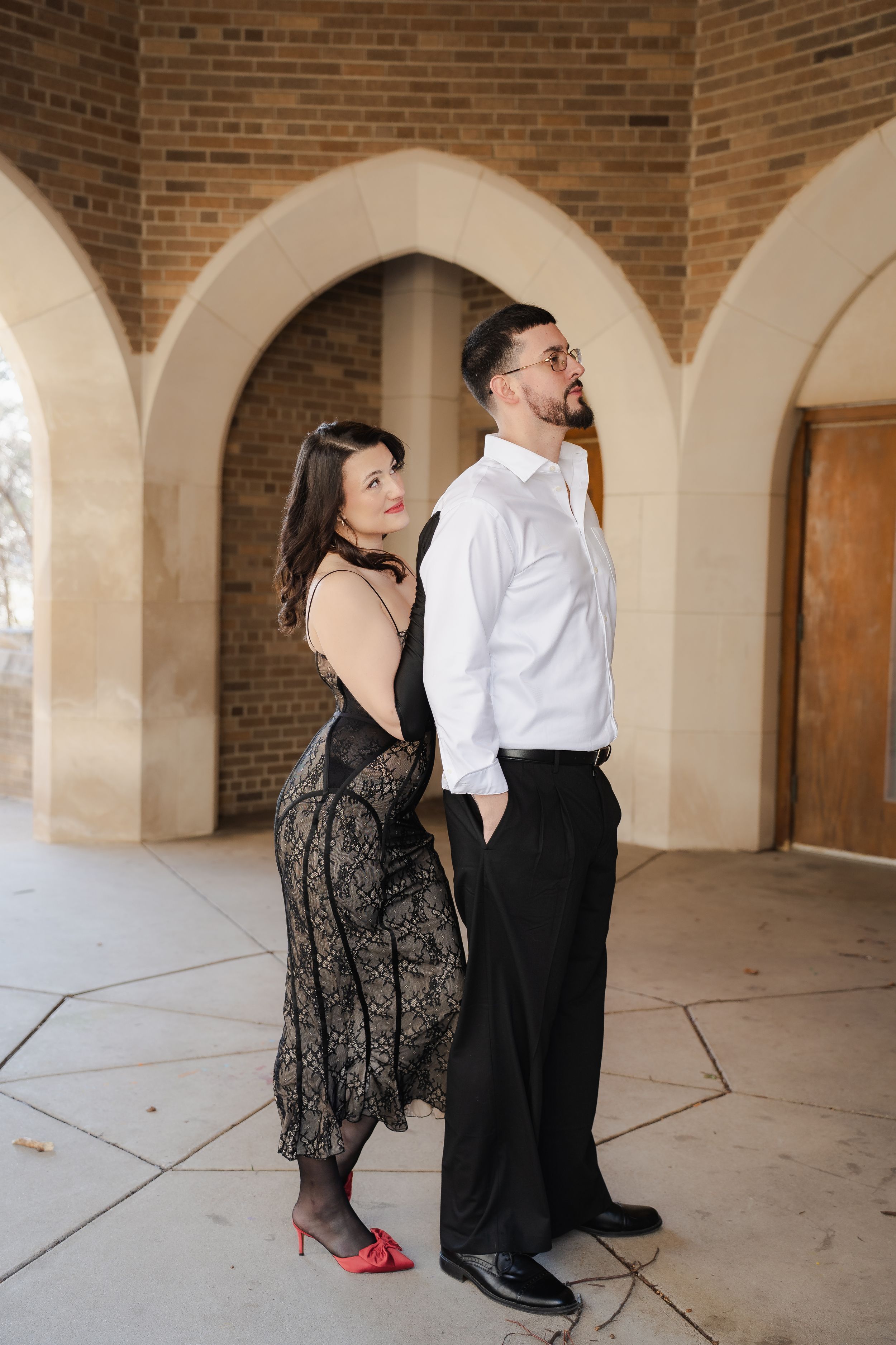 A couple dances romantically under arched brick columns in an elegant architectural setting.