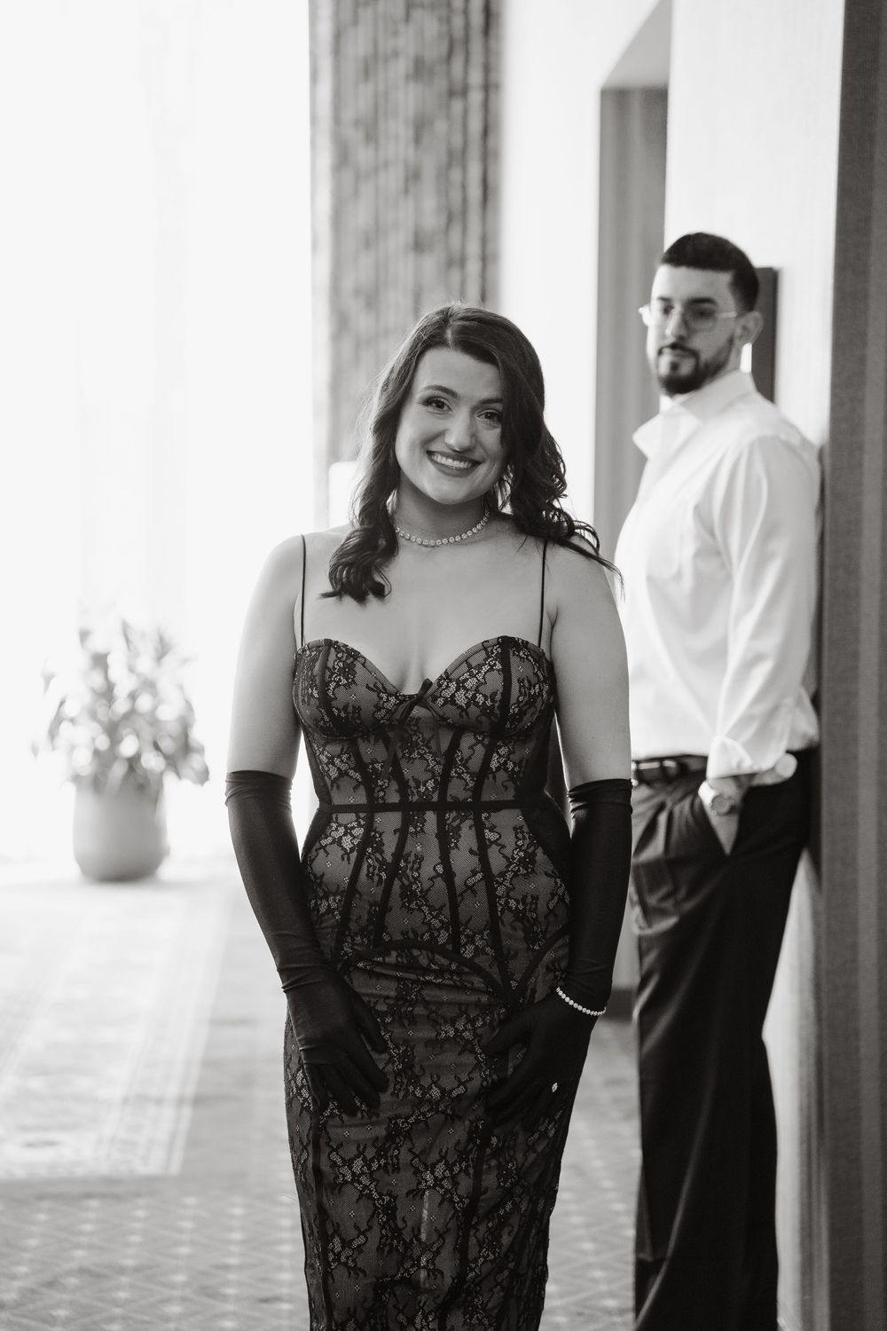 Black and white portrait of a couple in formal attire posing in an elegant indoor setting.