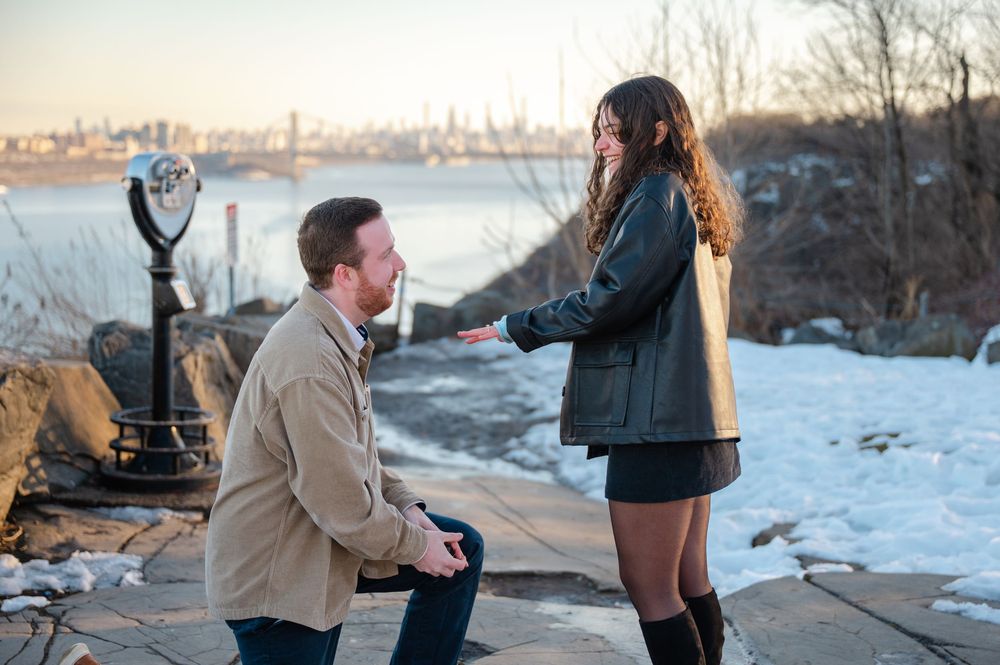 A couple shares a romantic moment during a winter engagement photoshoot with a scenic city skyline in the background.