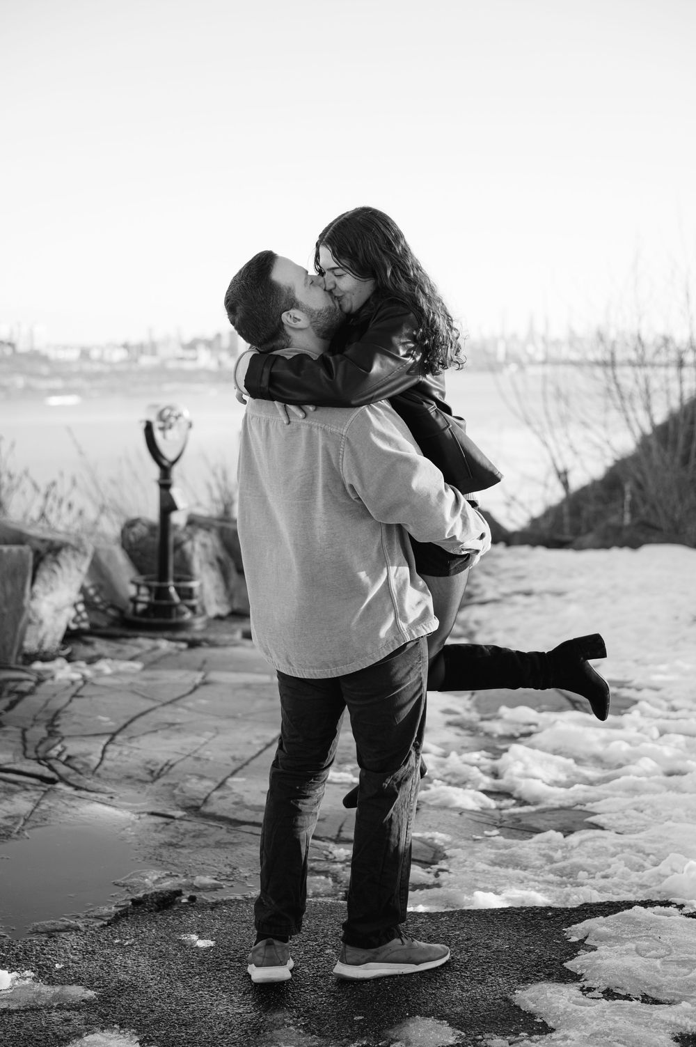 Black and white photos capture a couple's playful dance moves and romantic moments on a snowy beach.