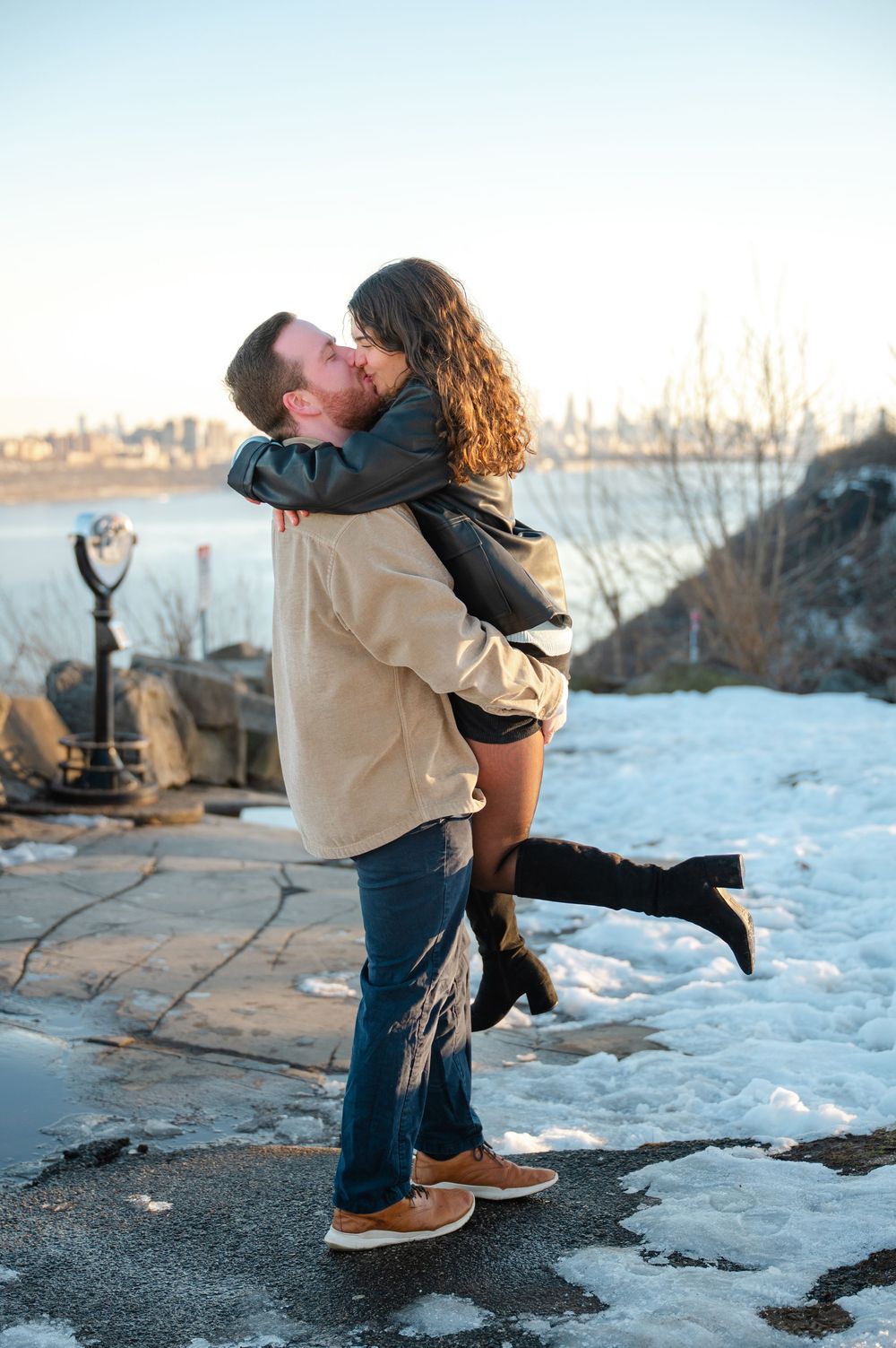 A romantic dip pose captured during an outdoor photoshoot with snowy landscape and water views.