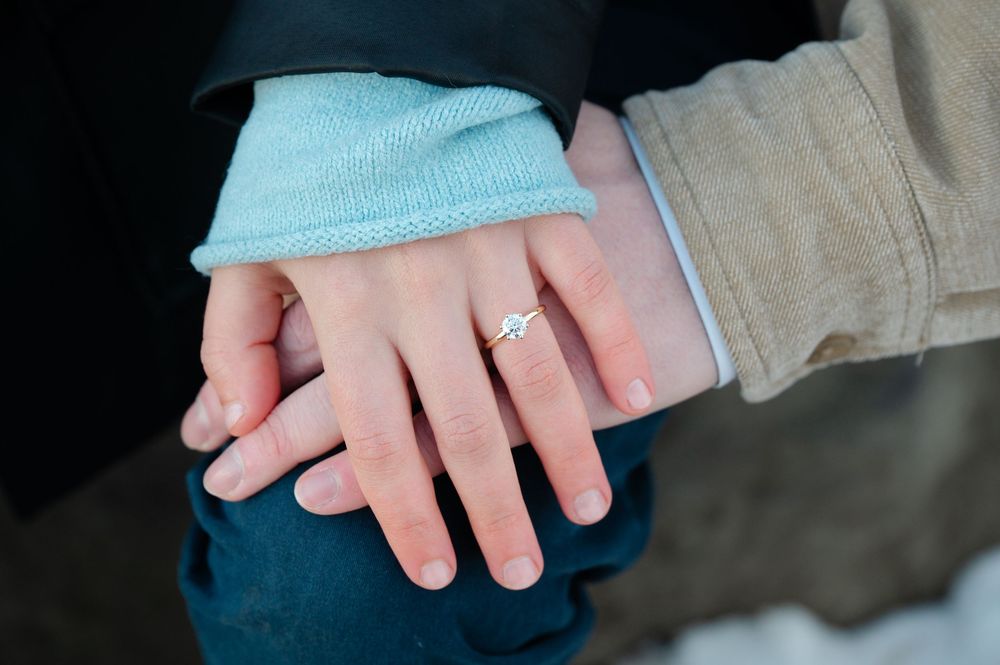 Close-up view of hands displaying an engagement ring with a sparkling diamond on a light background.