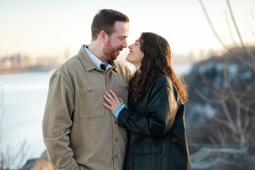 A couple shares a romantic moment at sunset in a winter outdoor setting while wearing warm coats.
