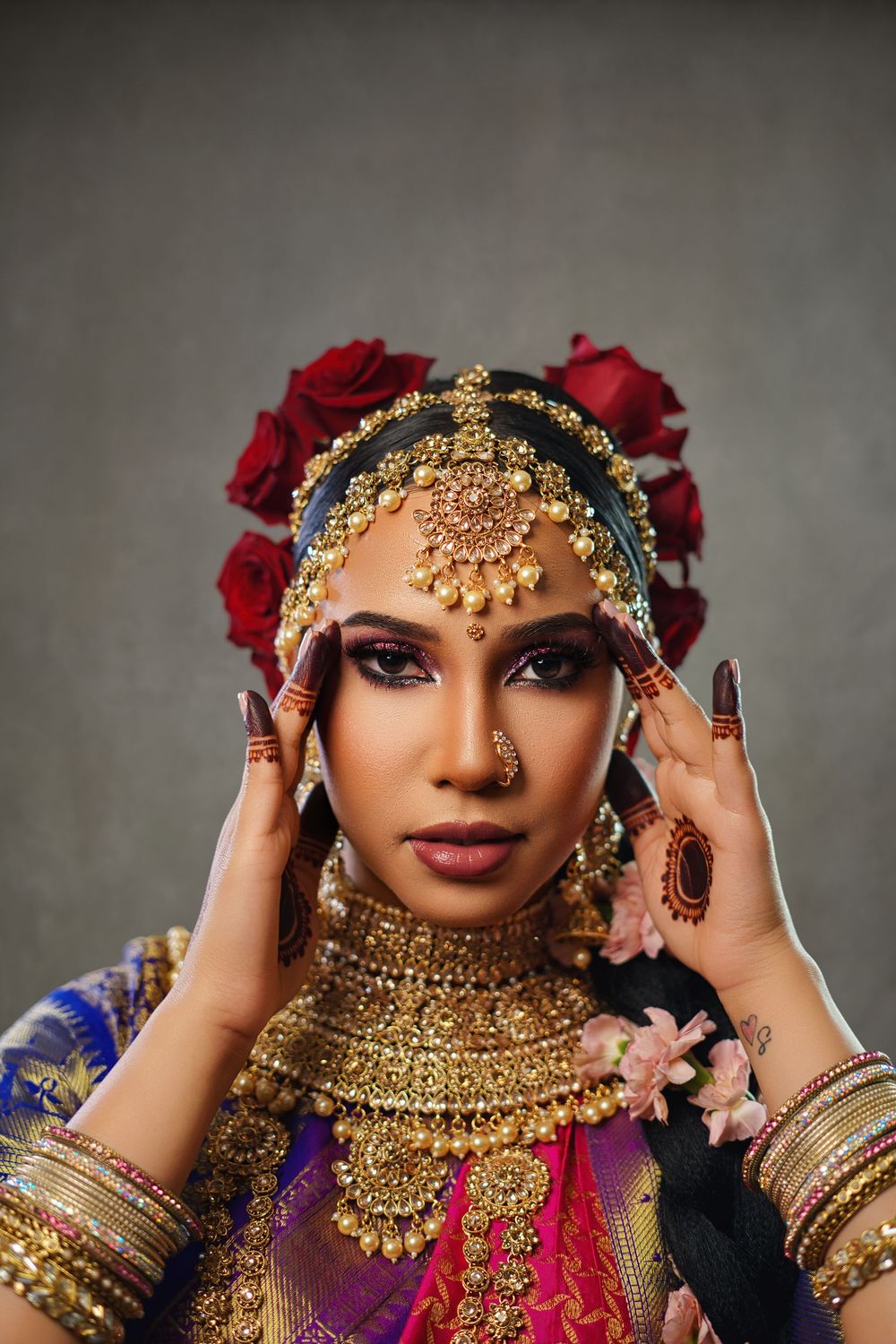 Traditional South Asian bridal look with ornate gold jewelry, red roses, and purple silk attire.