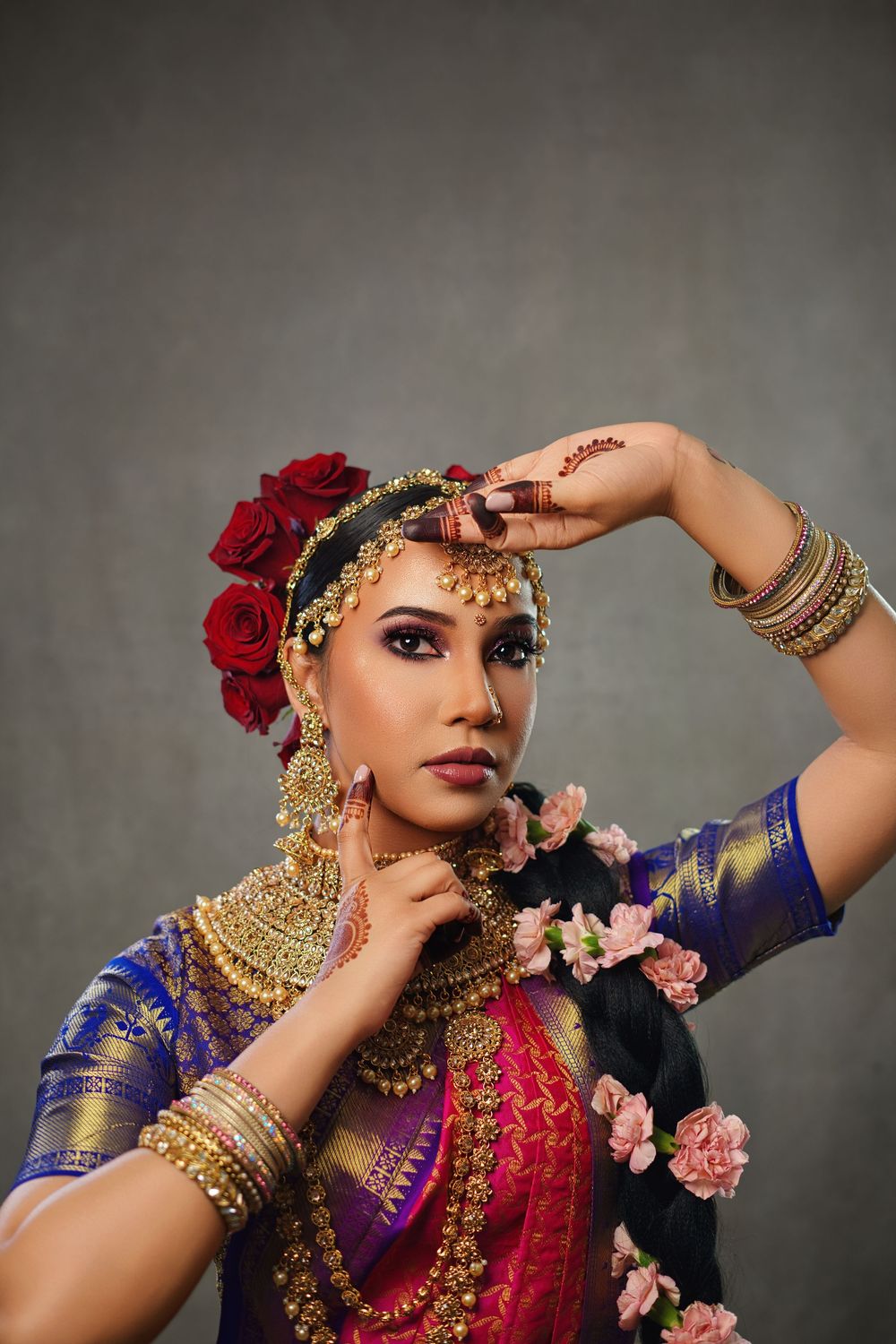 Traditional Indian bridal portrait featuring ornate gold jewelry, red roses, and a royal blue outfit against a dark backdrop.