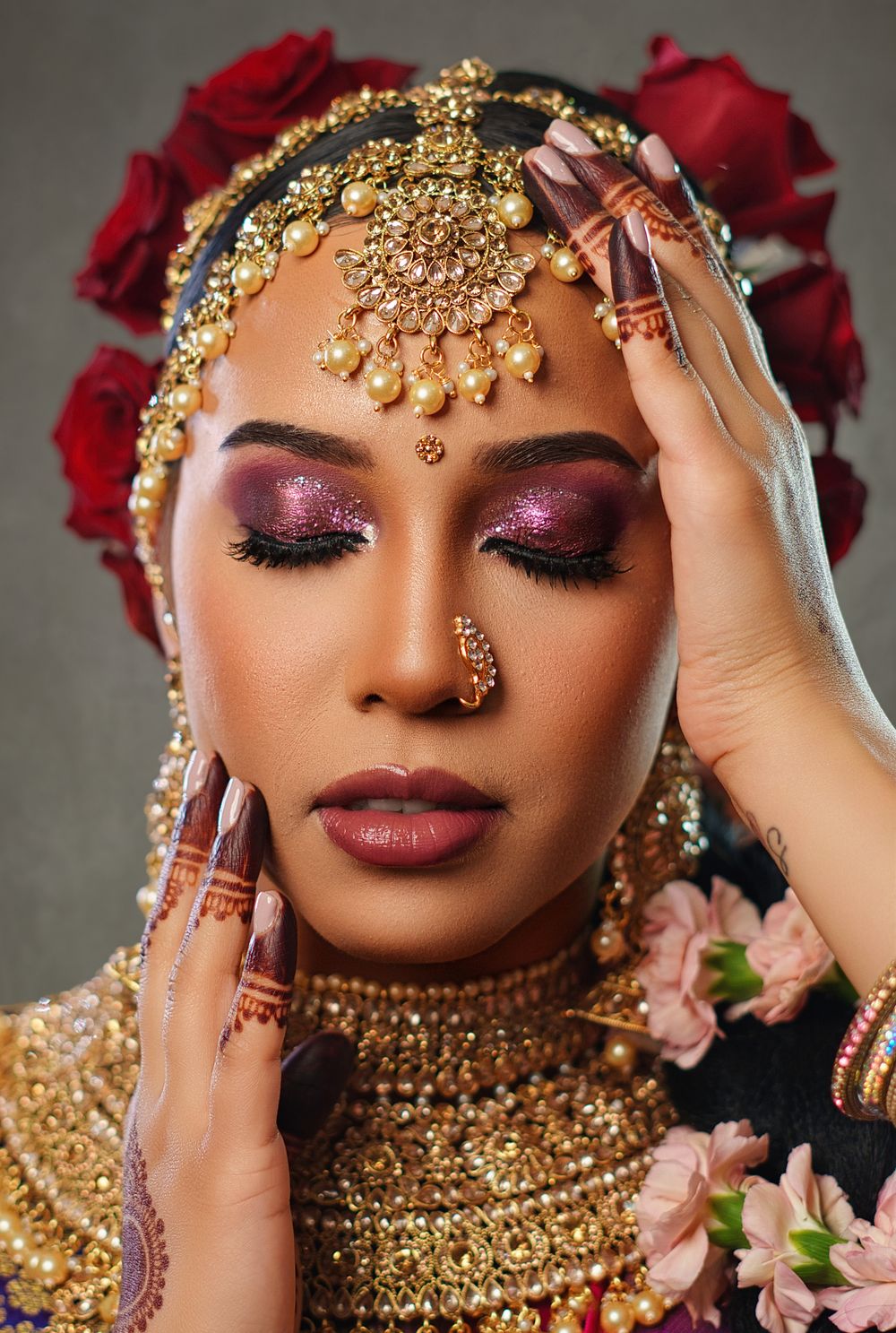 Close up of intricate bridal makeup with gold headpiece, henna designs and red roses.