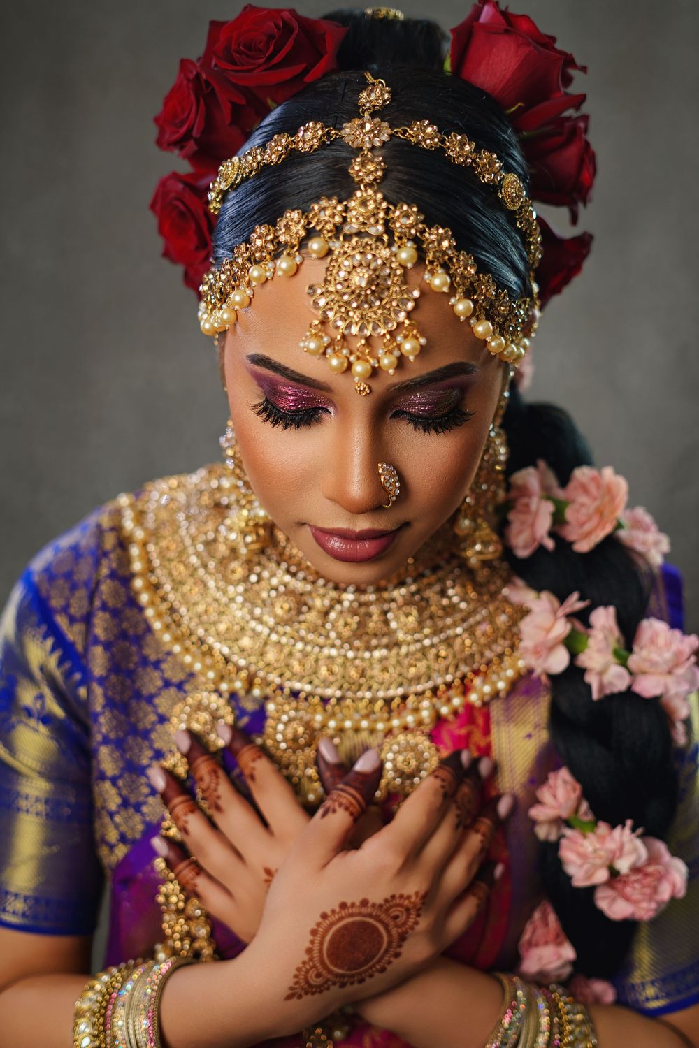 Traditional Indian bridal portrait featuring ornate gold jewelry, red roses, and blue attire with delicate henna designs.