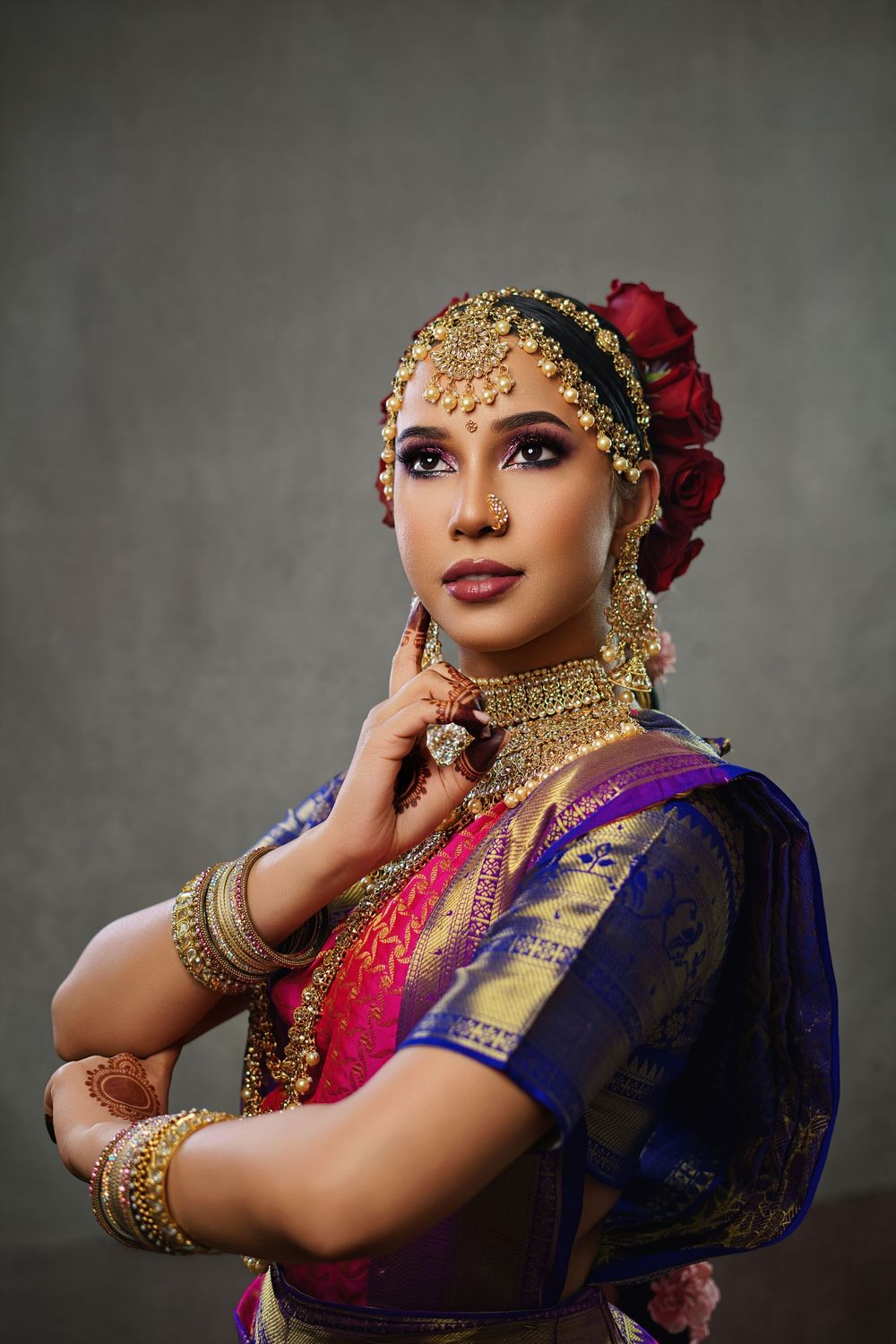 Portrait of dancer in purple and gold silk sari with intricate jewelry and red roses in hair.