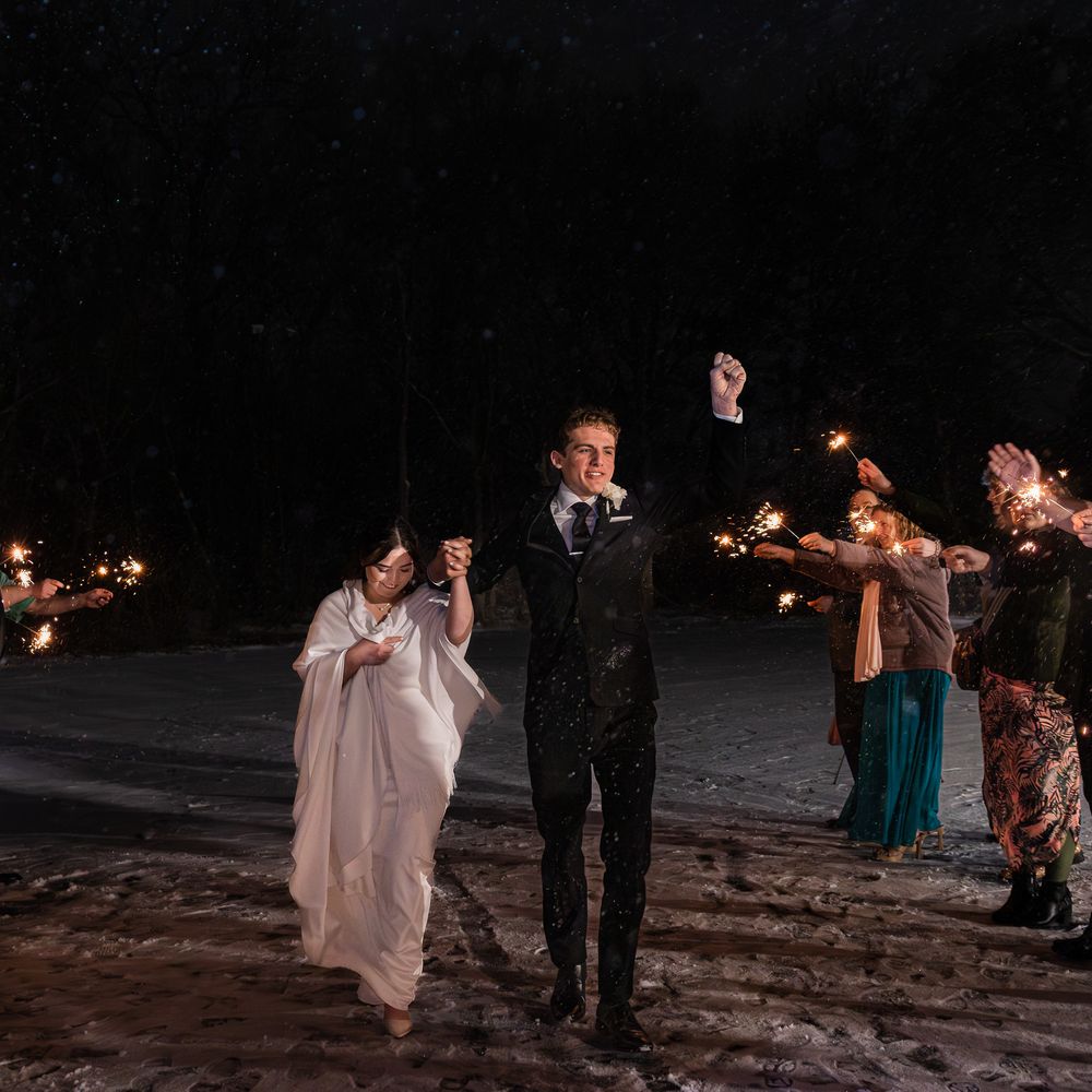 A couple celebrates with sparklers at their nighttime winter wedding surrounded by guests.