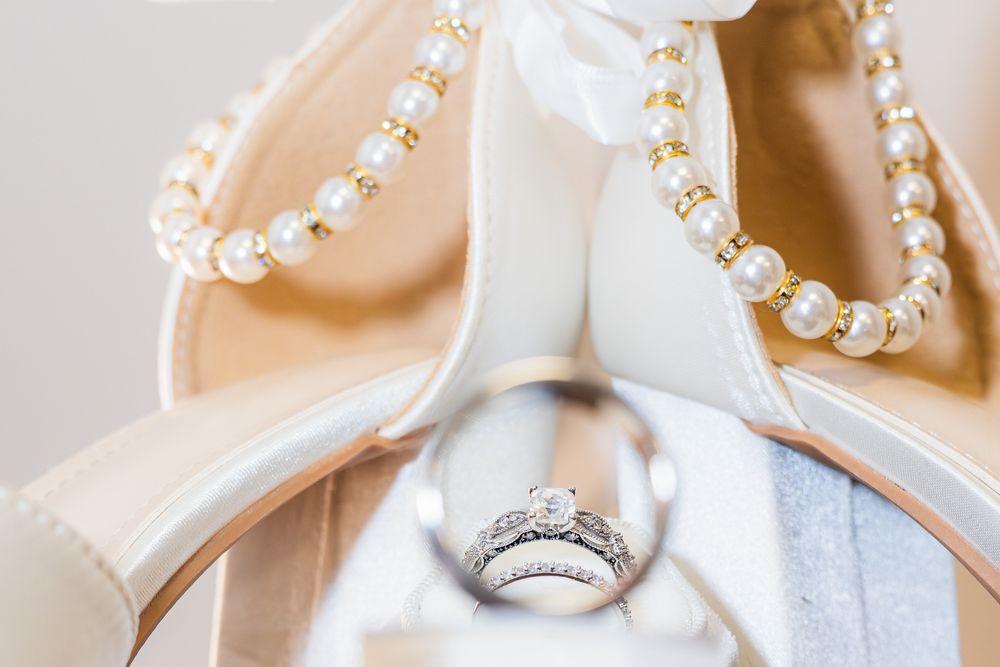 Wedding rings nestled between elegant white bridal shoes with pearl necklace accessories.