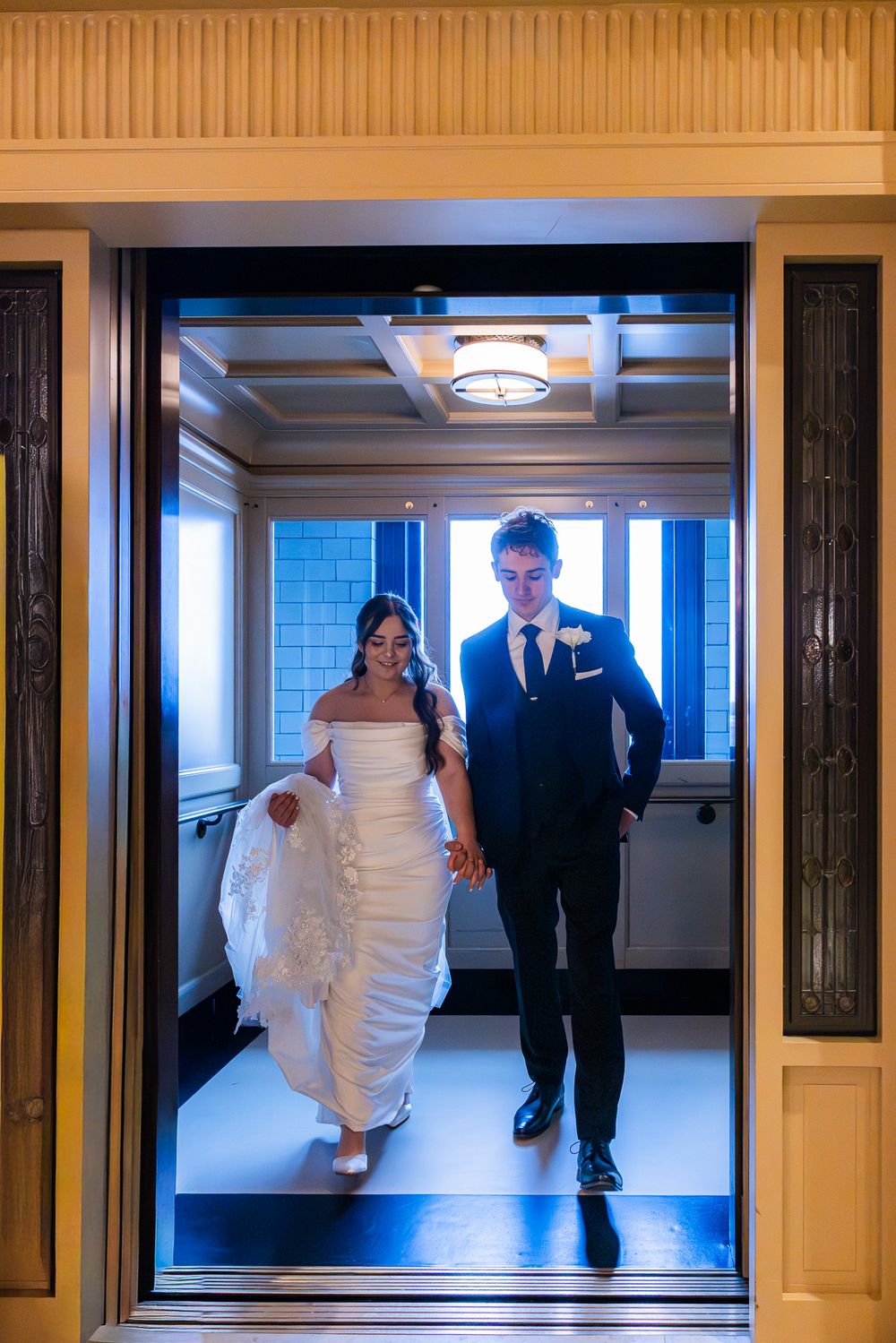 A couple walks through an elegant hallway with warm lighting during their wedding day.