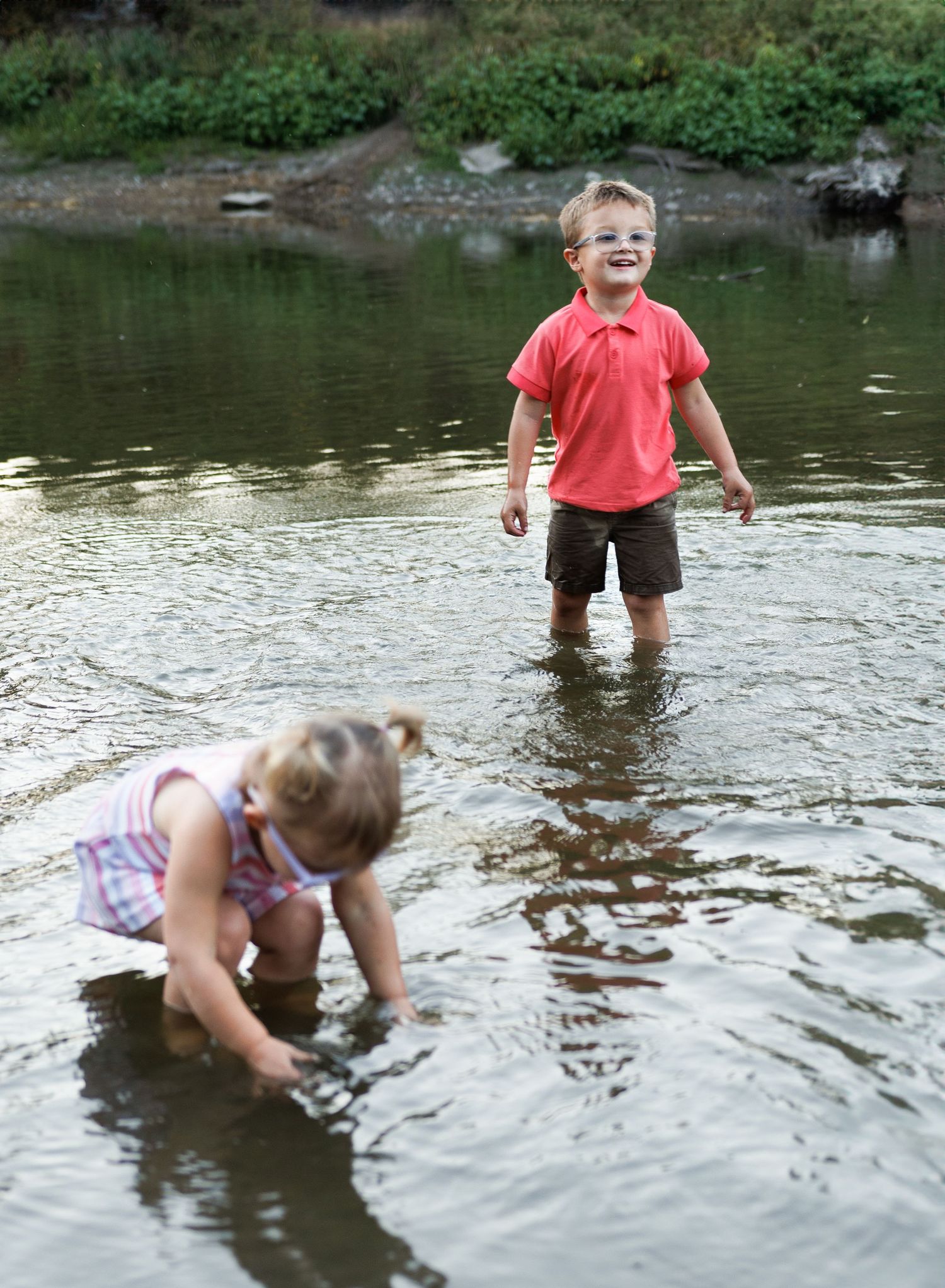 A sequence of people wading and splashing in a shallow pond or stream during a summer day.