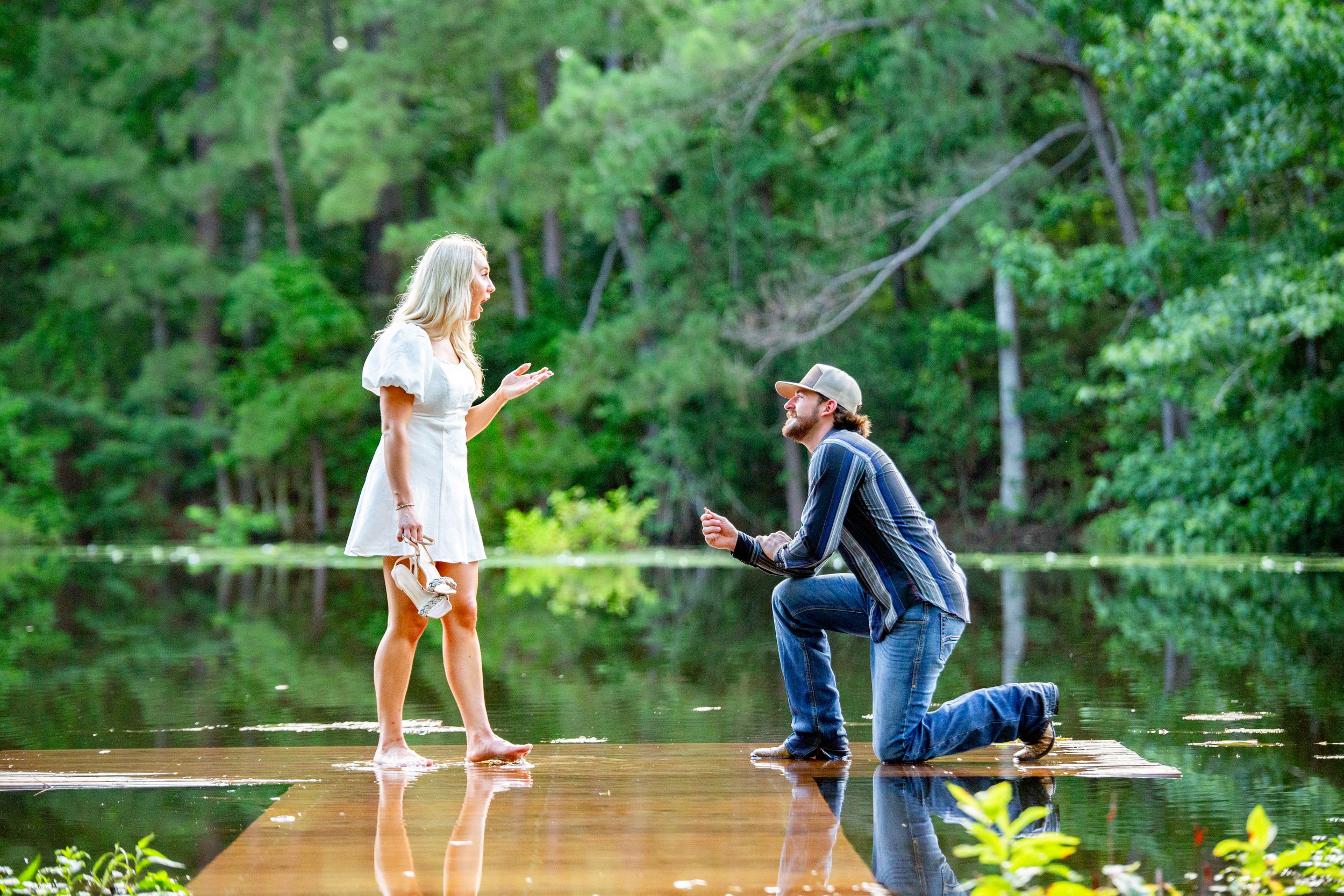 A couple enjoys a tender moment on a wooden dock surrounded by summer foliage.