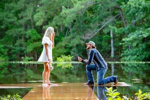 A couple shares an intimate moment on a lakeside dock during a sunny day.
