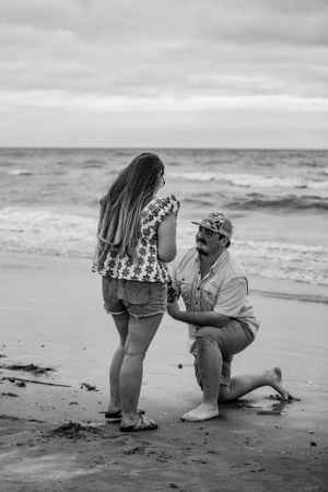 A black and white photo captures a proposal moment on a misty beach.
