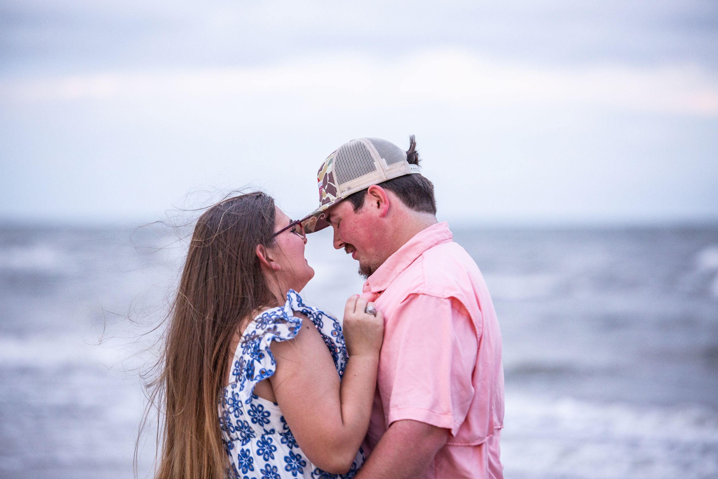 Romantic couple embraces on a beach at sunset wearing pink and blue patterned outfits.