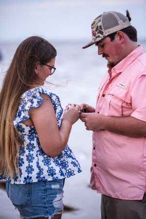 A couple shares an emotional moment on a beach wearing casual summer attire.