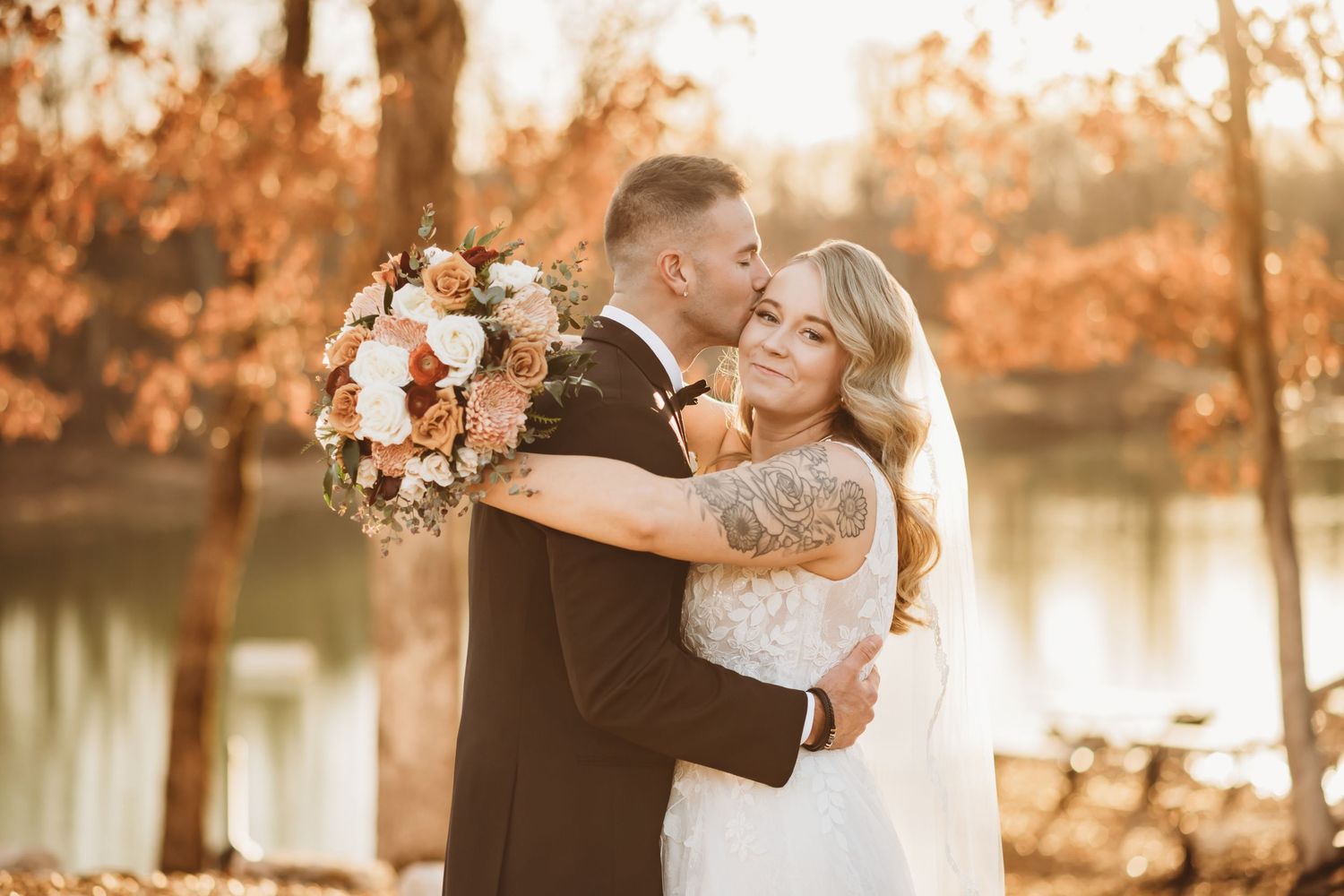 Groom kissing bride on her temple while the bride looks at the camera