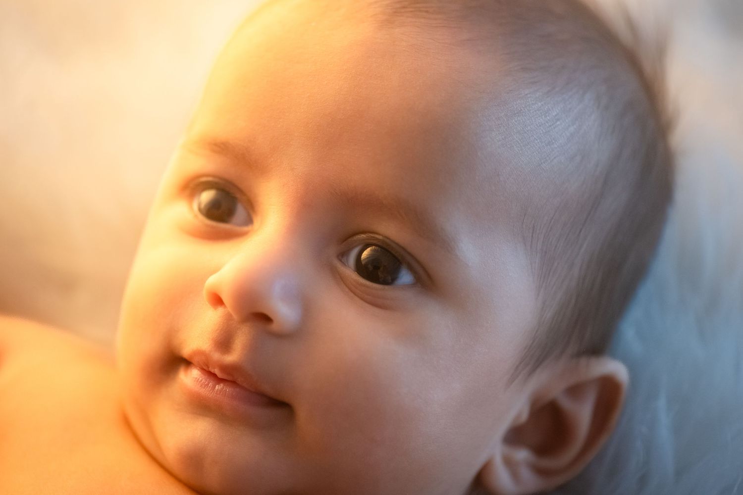A series of seven closeup portraits of a baby in warm lighting arranged in a horizontal row.