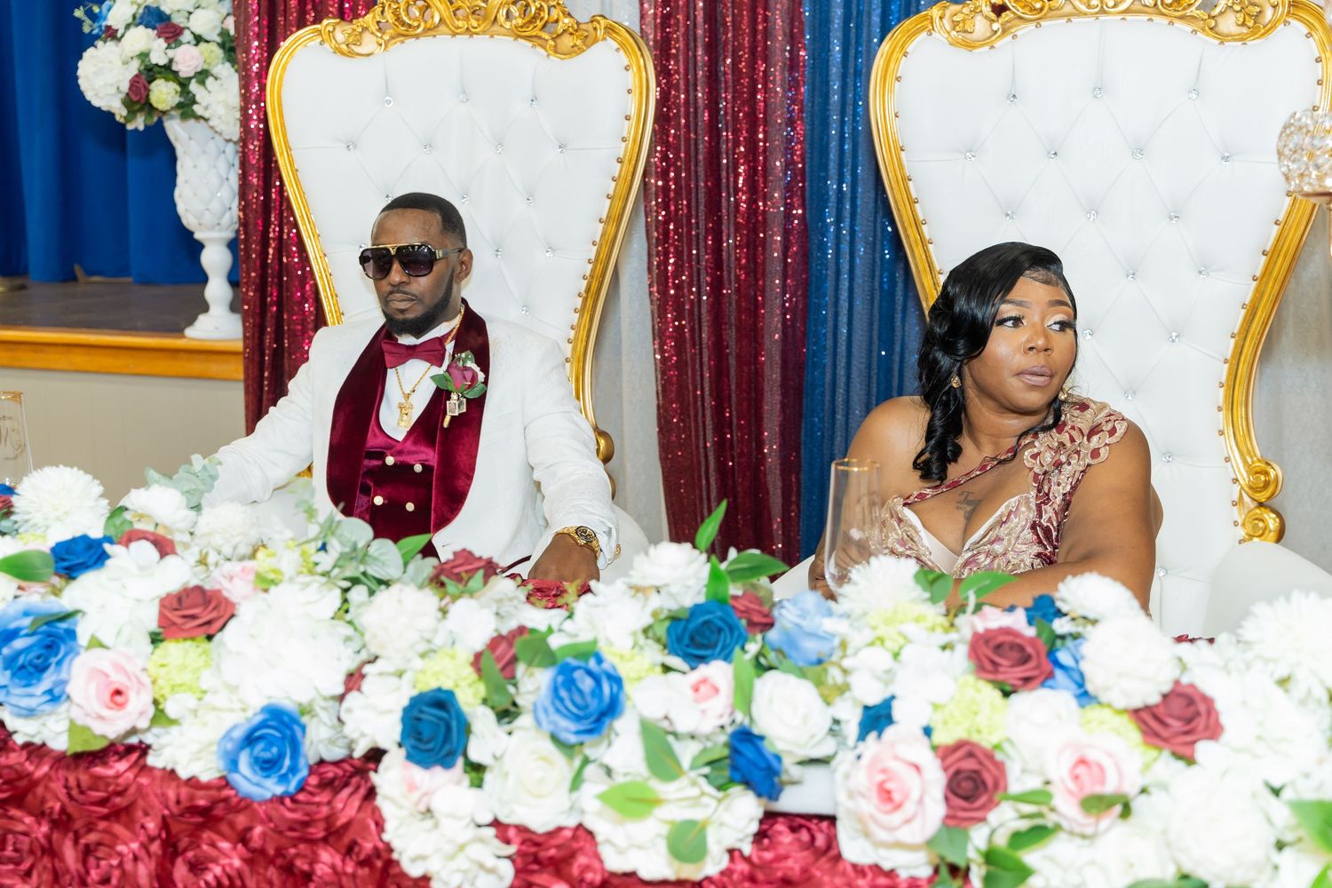 Ornate gold and white wedding throne chairs decorated with colorful floral arrangements at a formal celebration.